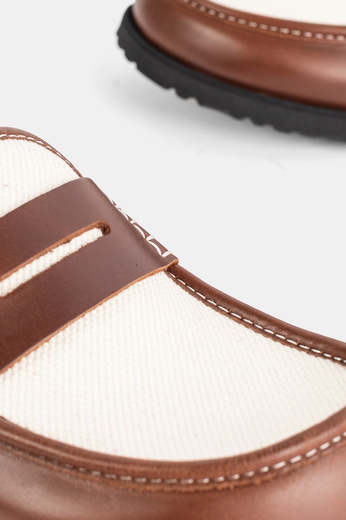 Detail van de Birkenstock 1774 Naples mule met kaneelkleurige pennyband op ecru vilt en lichte stiksels.