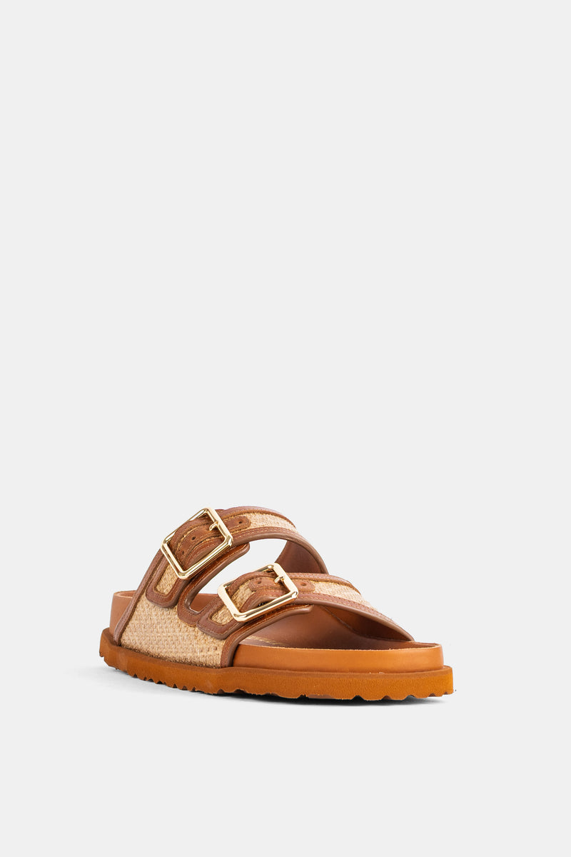 Mules donna Birkenstock 1774 in pelle cognac e rafia naturale, con fibbie quadrate dorate, vista di tre quarti.
