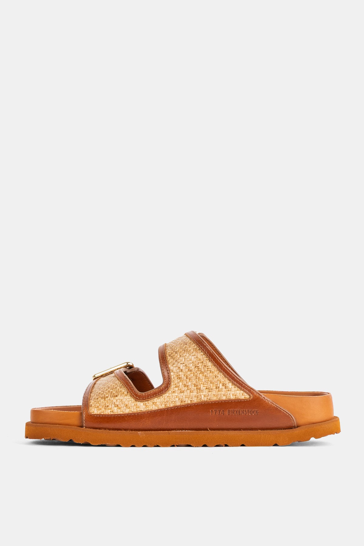 Mules Arizona Birkenstock 1774 di profilo con cinturino in rafia beige, bordo cognac e suola carrarmato camel.