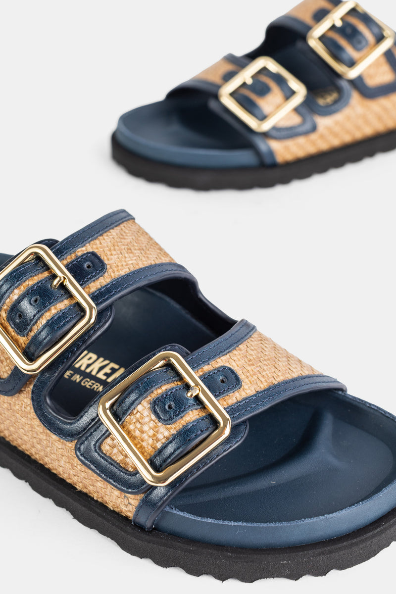 Dettaglio sandali Birkenstock 1774 Arizona con grandi fibbie dorate su cinturini in pelle navy e rafia