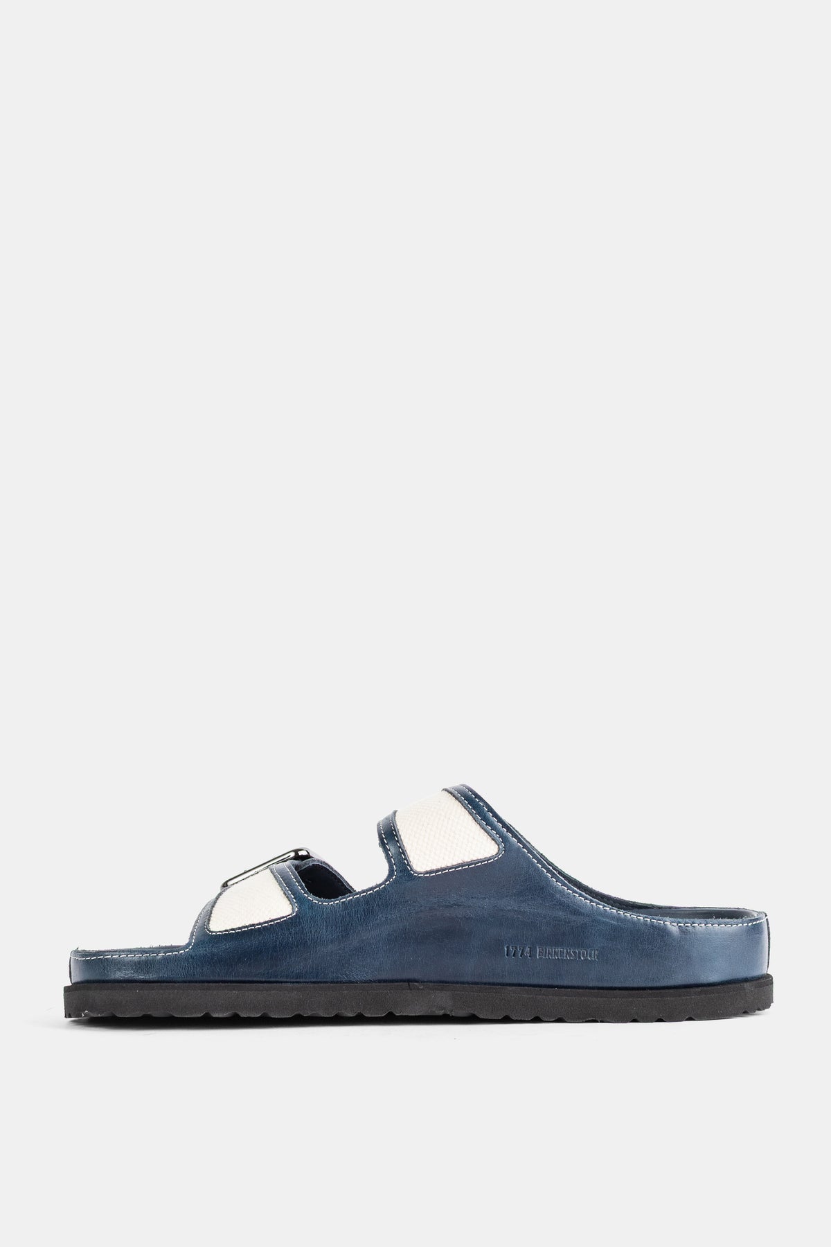 Sabot uomo Birkenstock 1774 profilo laterale, tomaia in pelle blu notte e cinturini in tela crema su suola nera