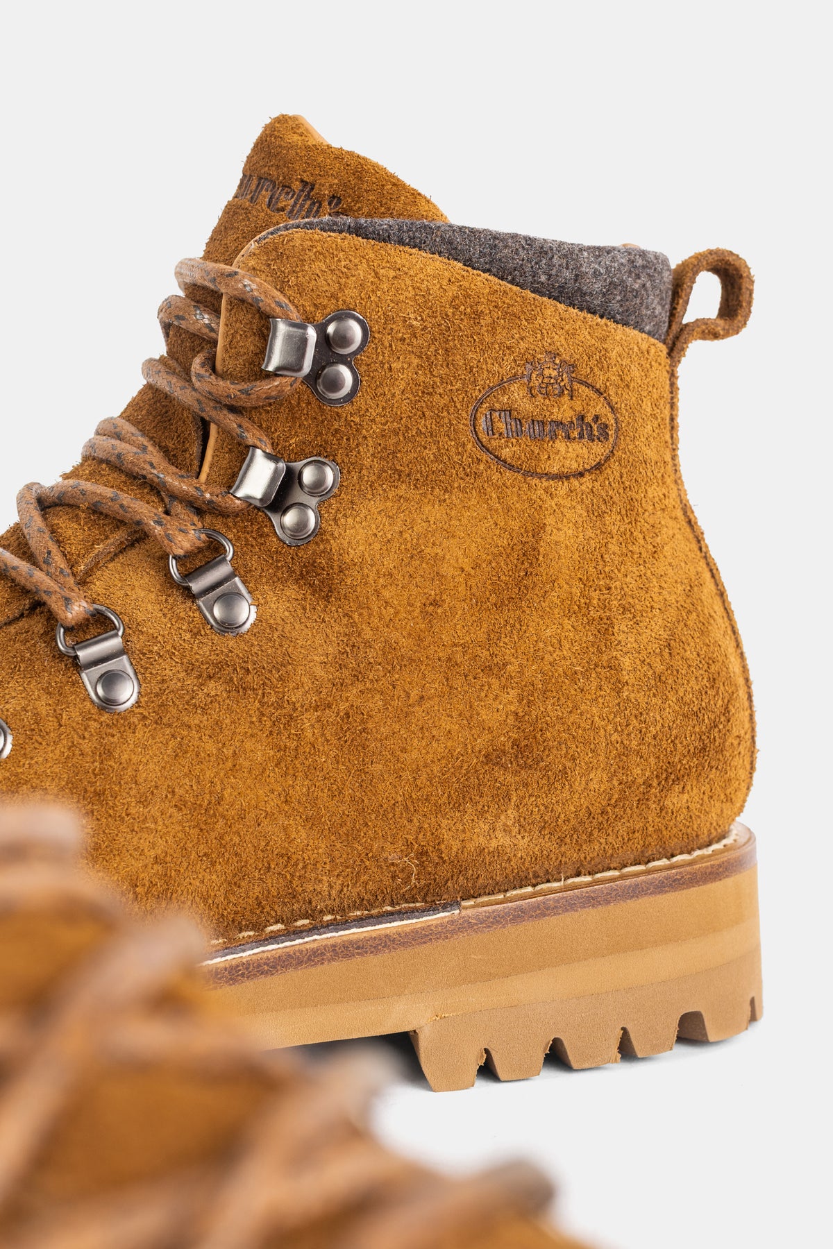 Close-up of Church's boot in tawny suede, showing the oval embossed logo and slate gray felted collar.