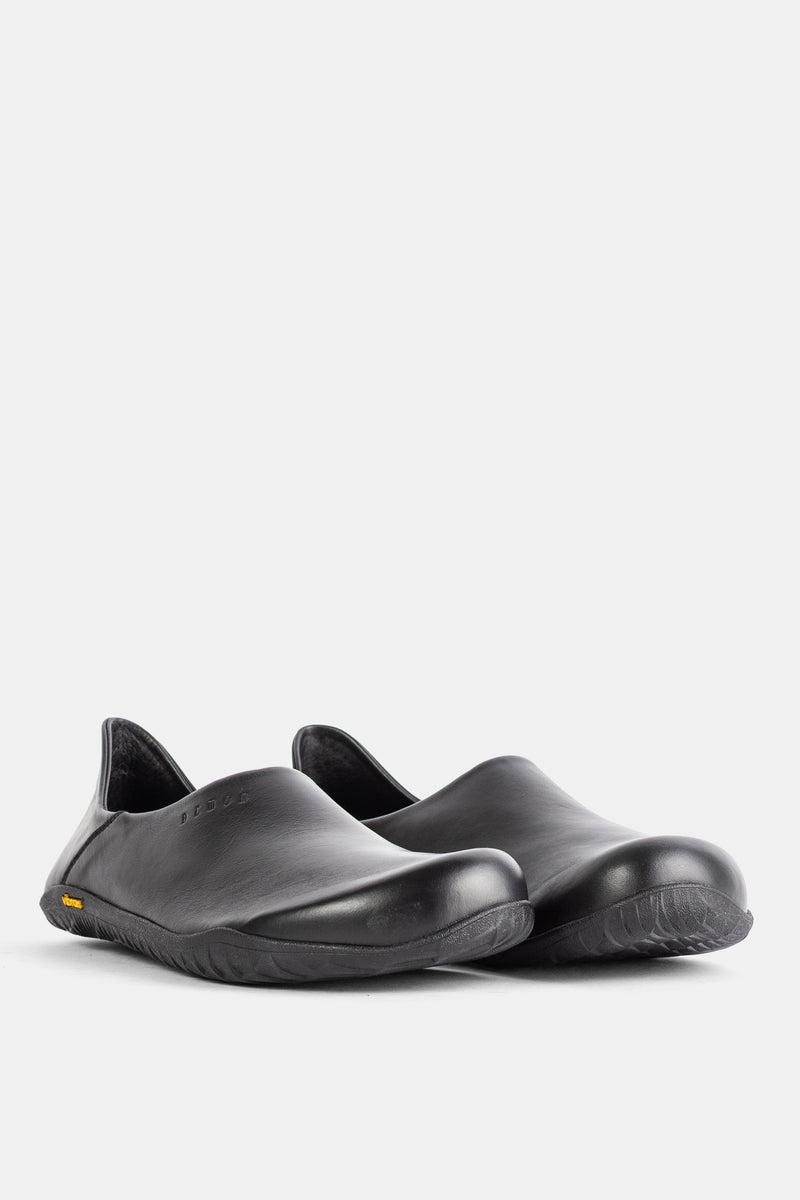 A pair of Demon Dalmara shiny black leather mules featuring an embossed logo and yellow Vibram sole details.