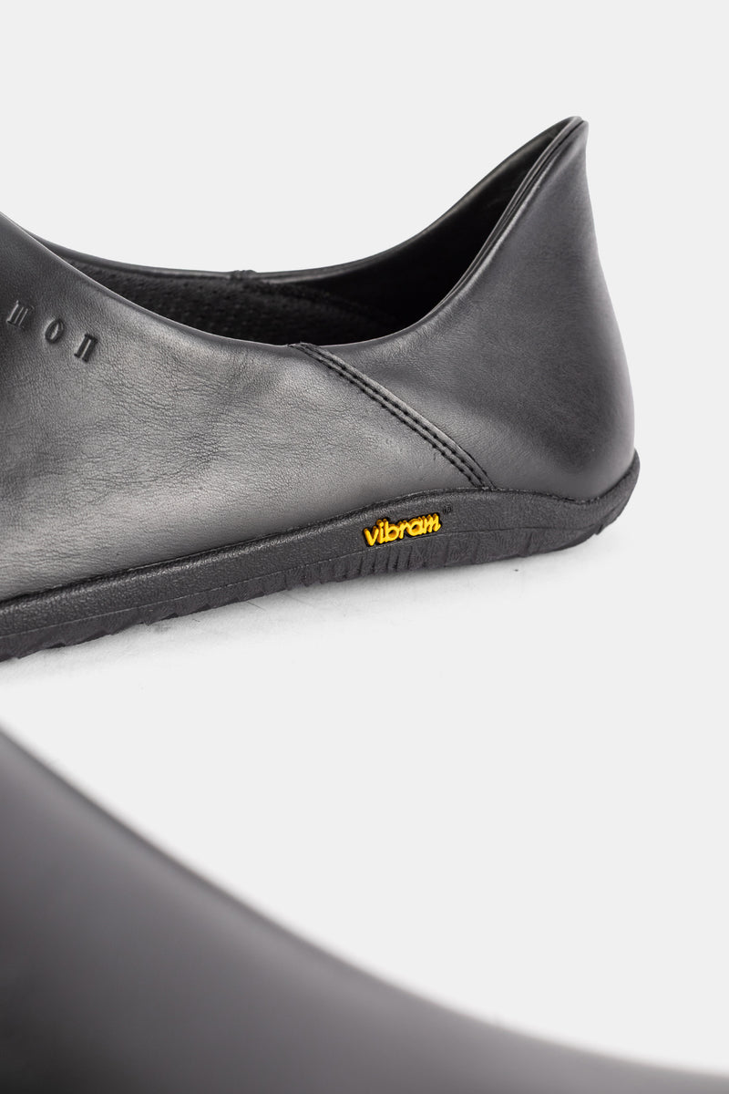 Rear heel view of the Demon Dalmara black leather mule with yellow Vibram logo on a slim minimalist sole.