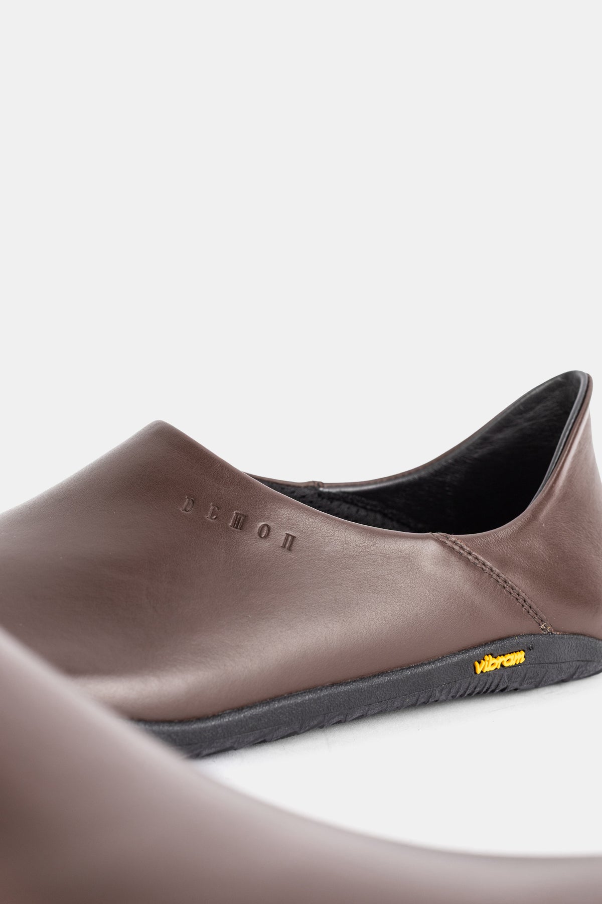 Gros plan talon mule Demon Dalmara homme, logo embossé cuir marron et étiquette Vibram jaune visible