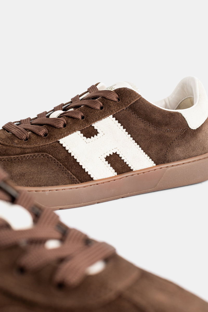 Dettaglio sneakers Hogan Cool uomo, camoscio marrone effetto velluto, patch H ecru smerlato e lacci cioccolato.