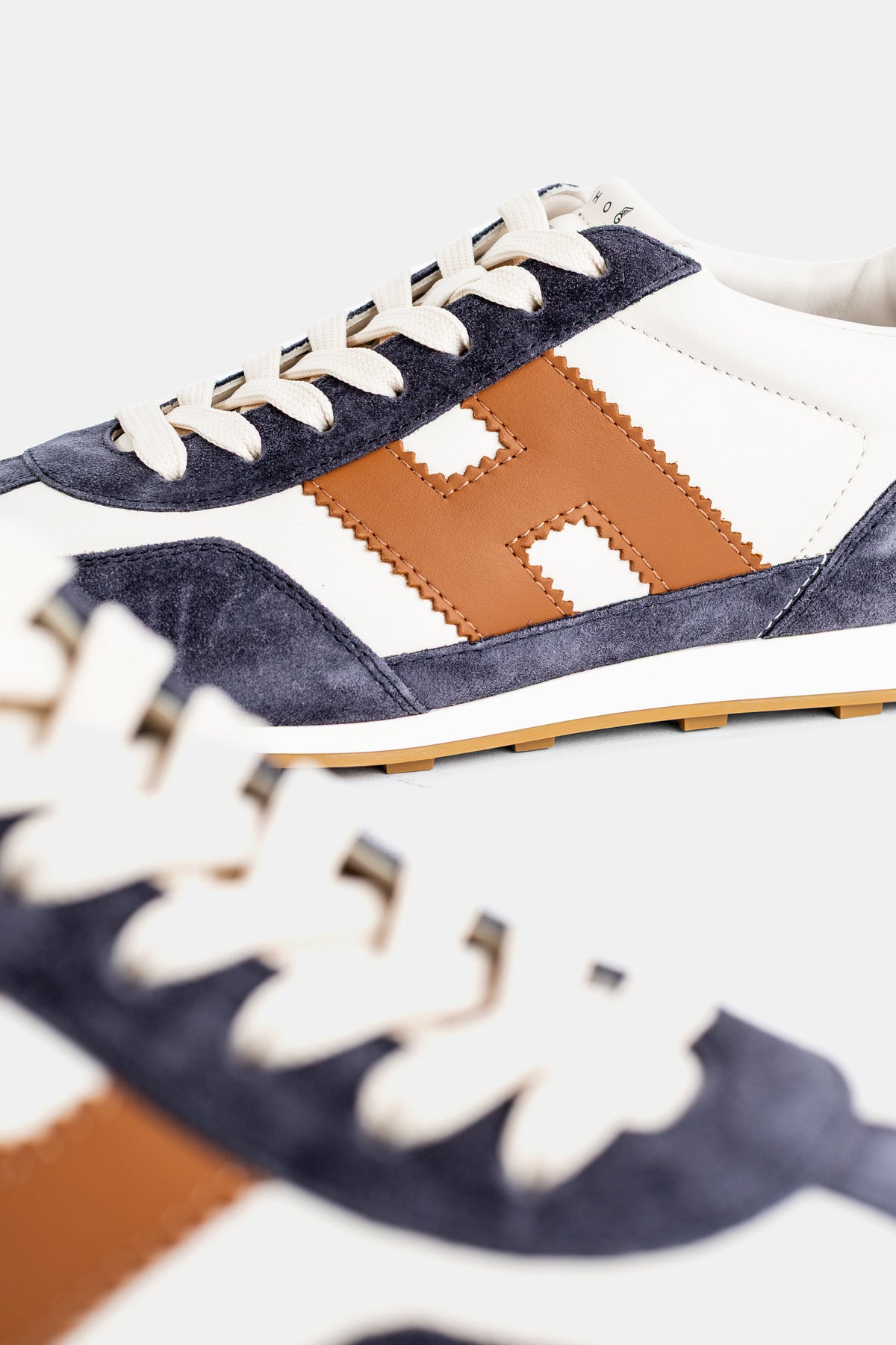 Hogan sneakers dettaglio logo H in pelle cammello e cuciture su fondo scamosciato blu notte e base bianca.