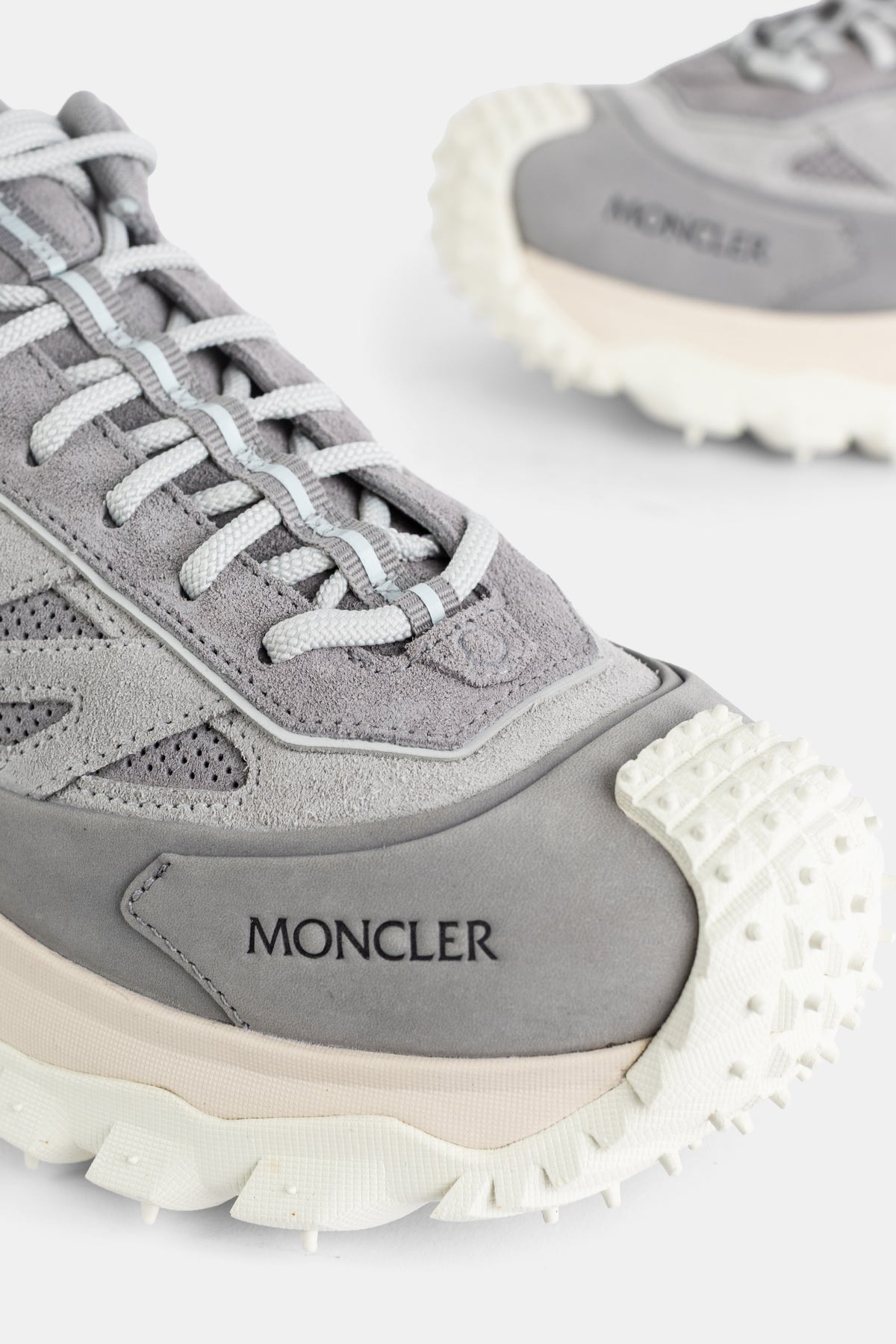 Grande plano frontal da sapatilha Moncler Trailgrip GTX cinzenta, logótipo em relevo e sola dentada branca