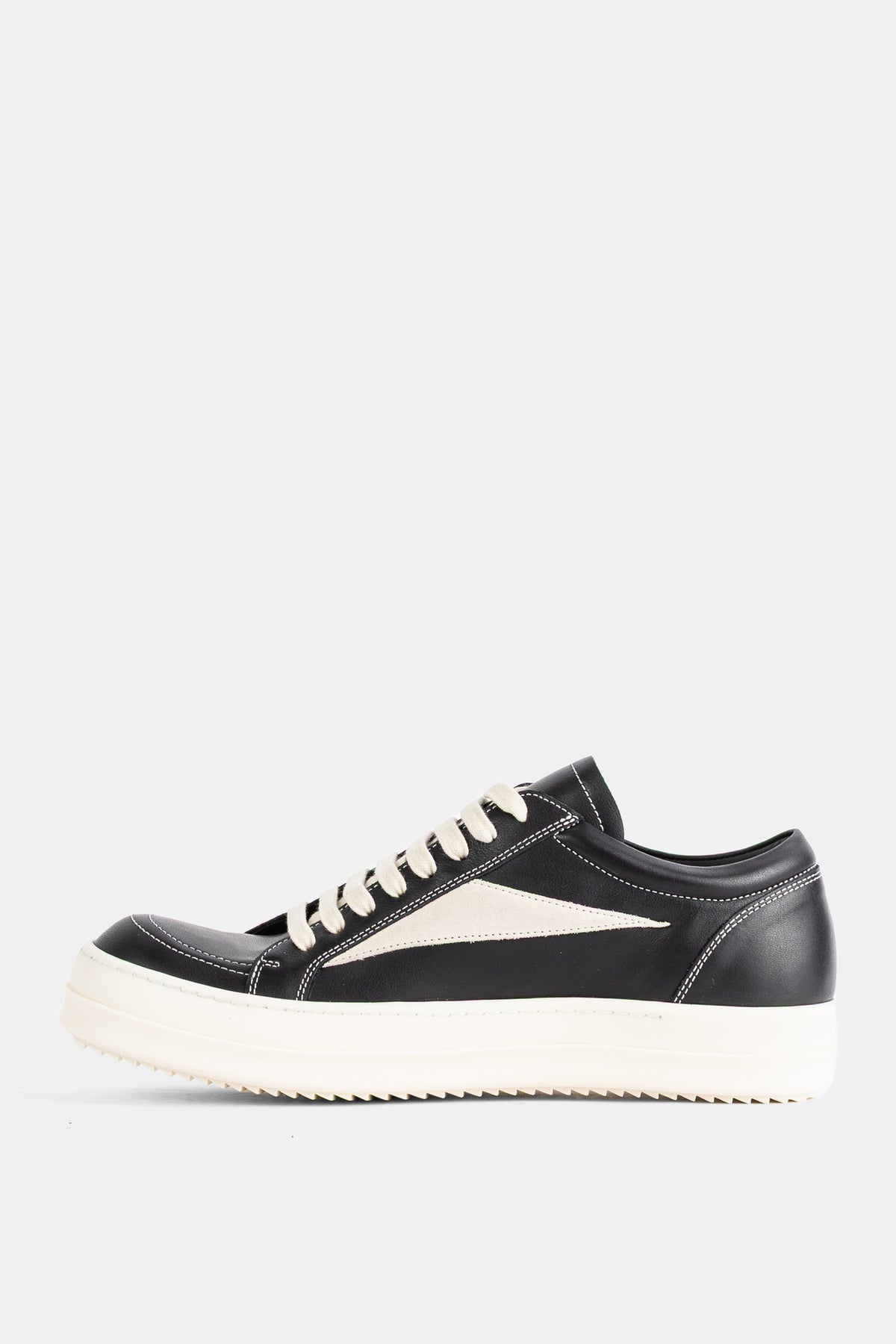 Rick Owens low-top sneakers in black leather with a white ridged sole and a triangular ivory side insert, profile view