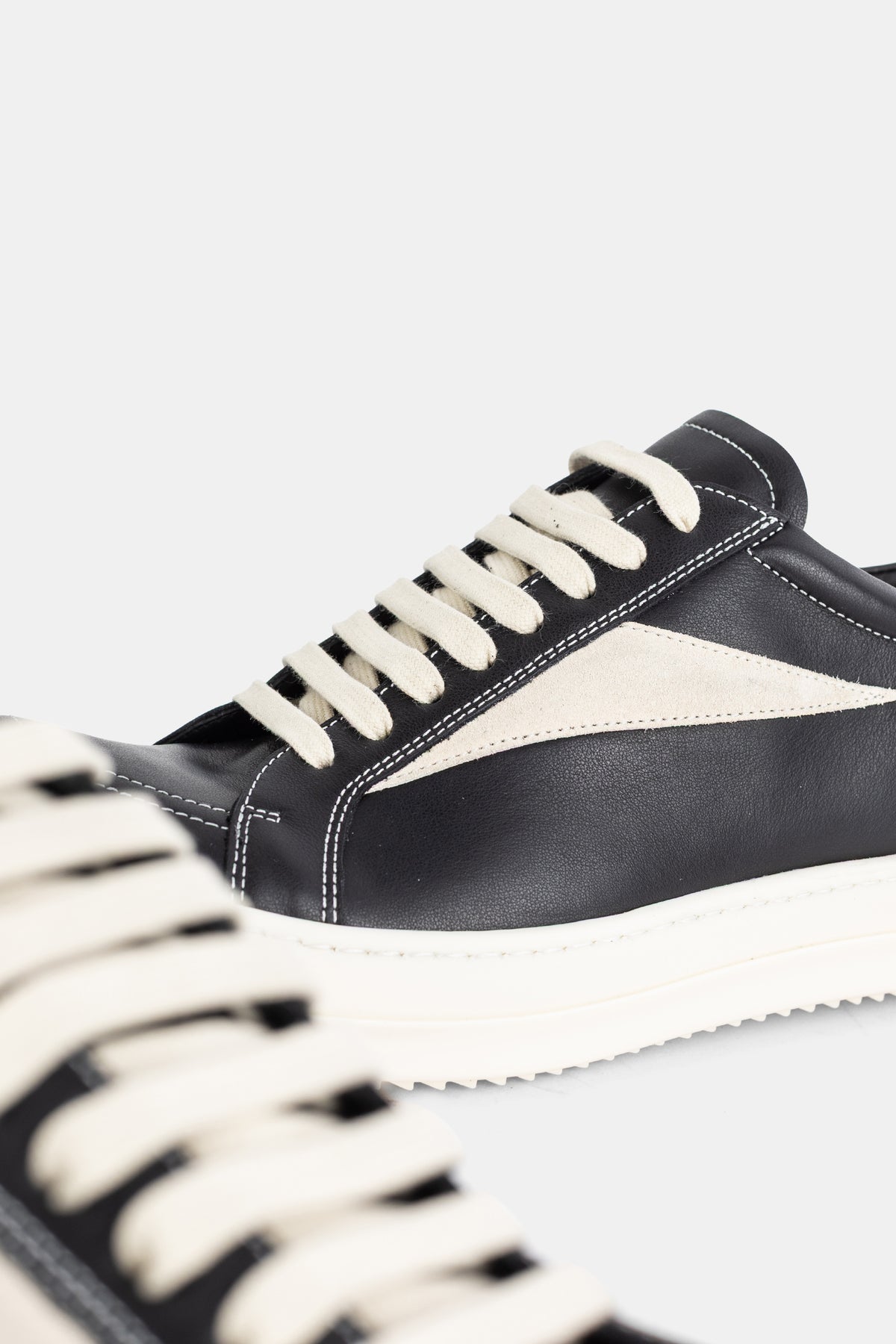 Rick Owens black leather sneakers close-up showing the contrasting topstitching and braided ecru cotton laces