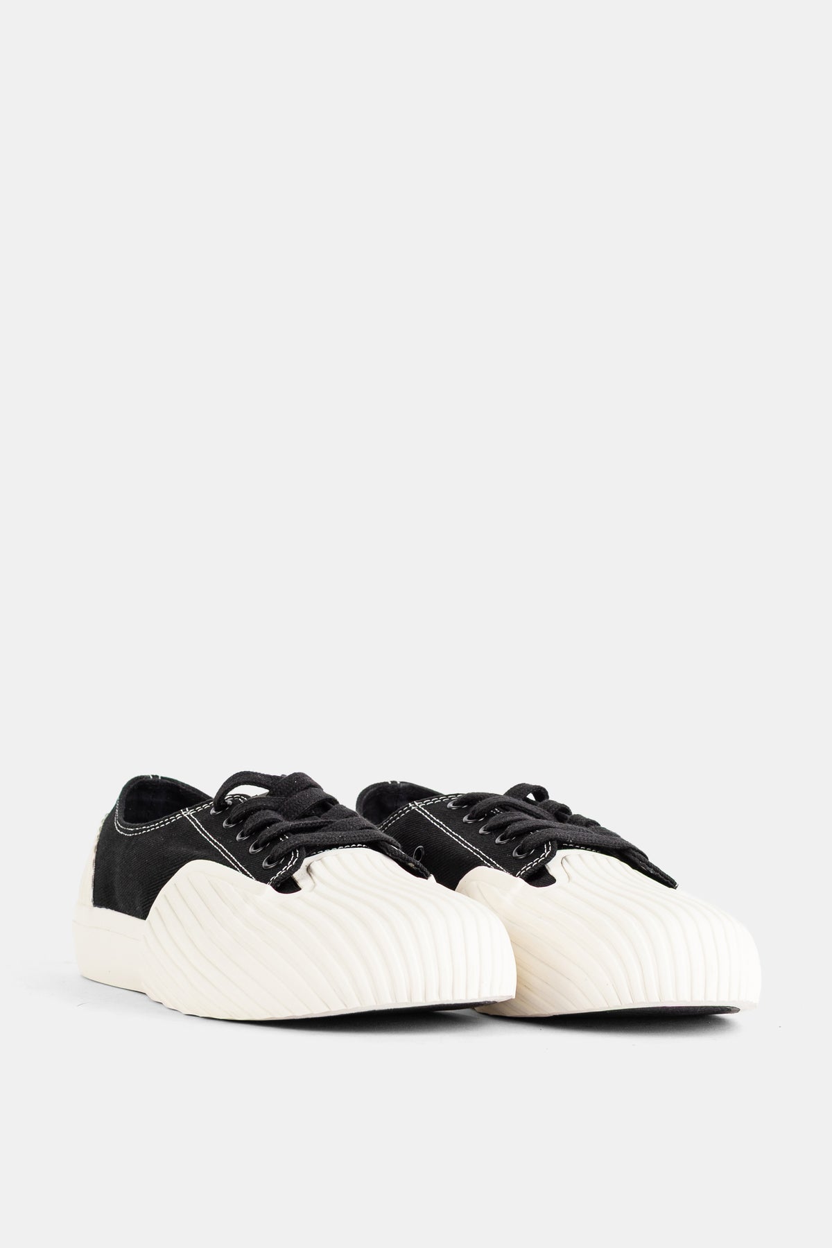 Frontansicht des Unformed Prototype 01 Sneakers mit schwarzen Schnürsenkeln und wellenartig strukturierter weißer Kappe.