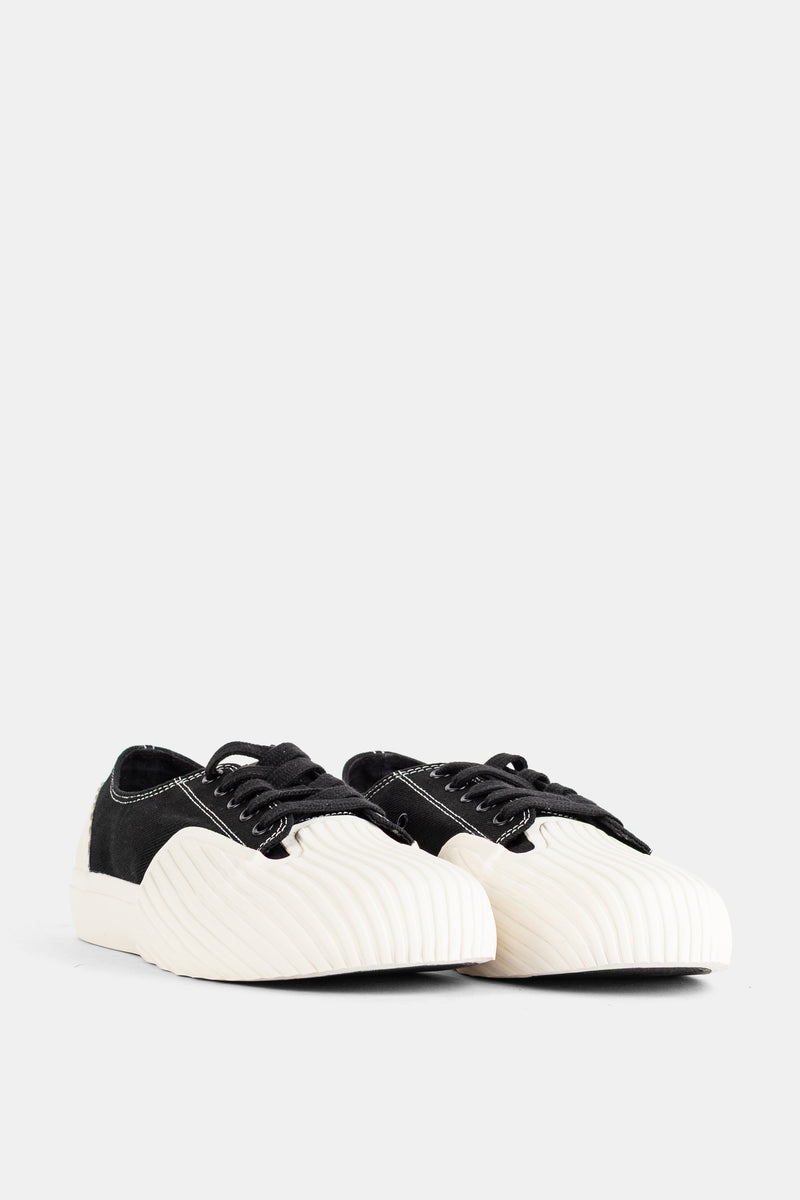Frontansicht des Unformed Prototype 01 Sneakers mit schwarzen Schnürsenkeln und wellenartig strukturierter weißer Kappe.