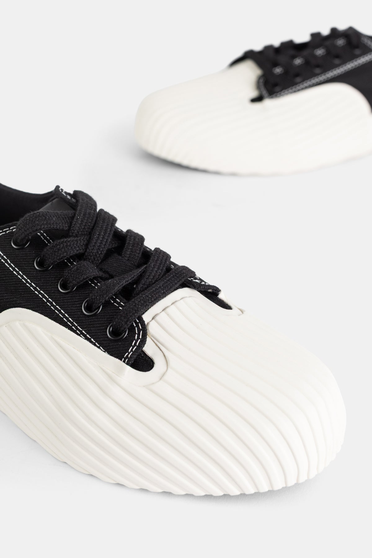 Nahaufnahme der weißen Rillensohle des Unformed Prototype 01 Sneakers aus schwarzem Canvas mit dicken Schnürsenkeln.