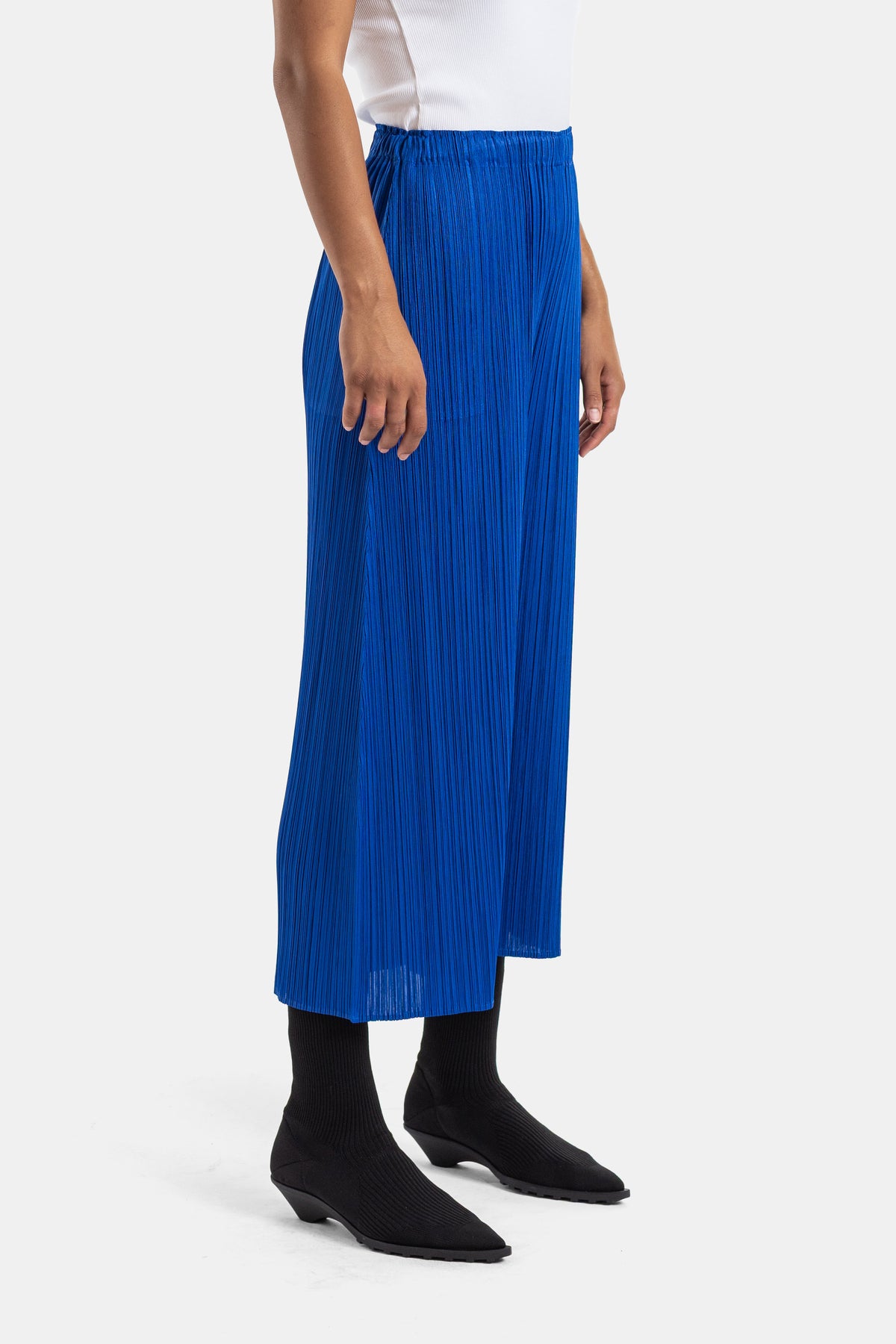 Pleats Please Issey Miyake plissé damesbroek in kobaltblauw, elegant zijaanzicht met zwarte enkellaarsjes.