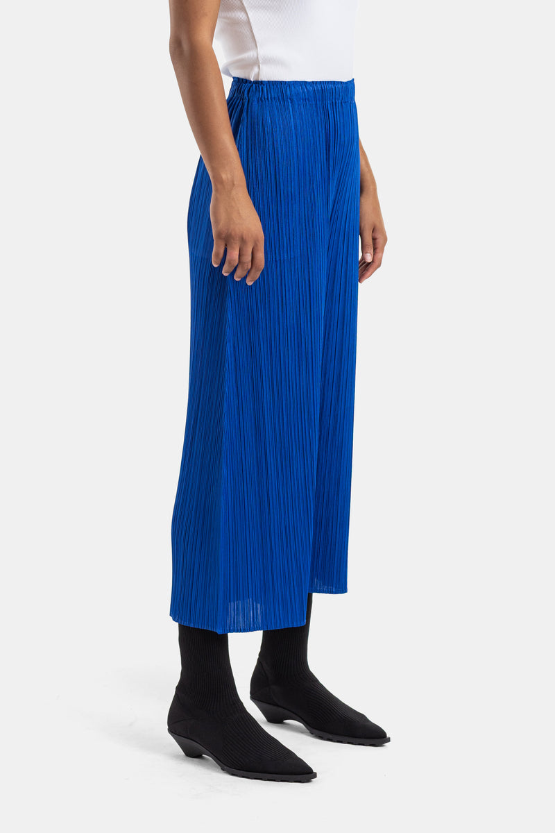 Pleats Please Issey Miyake plissé damesbroek in kobaltblauw, elegant zijaanzicht met zwarte enkellaarsjes.