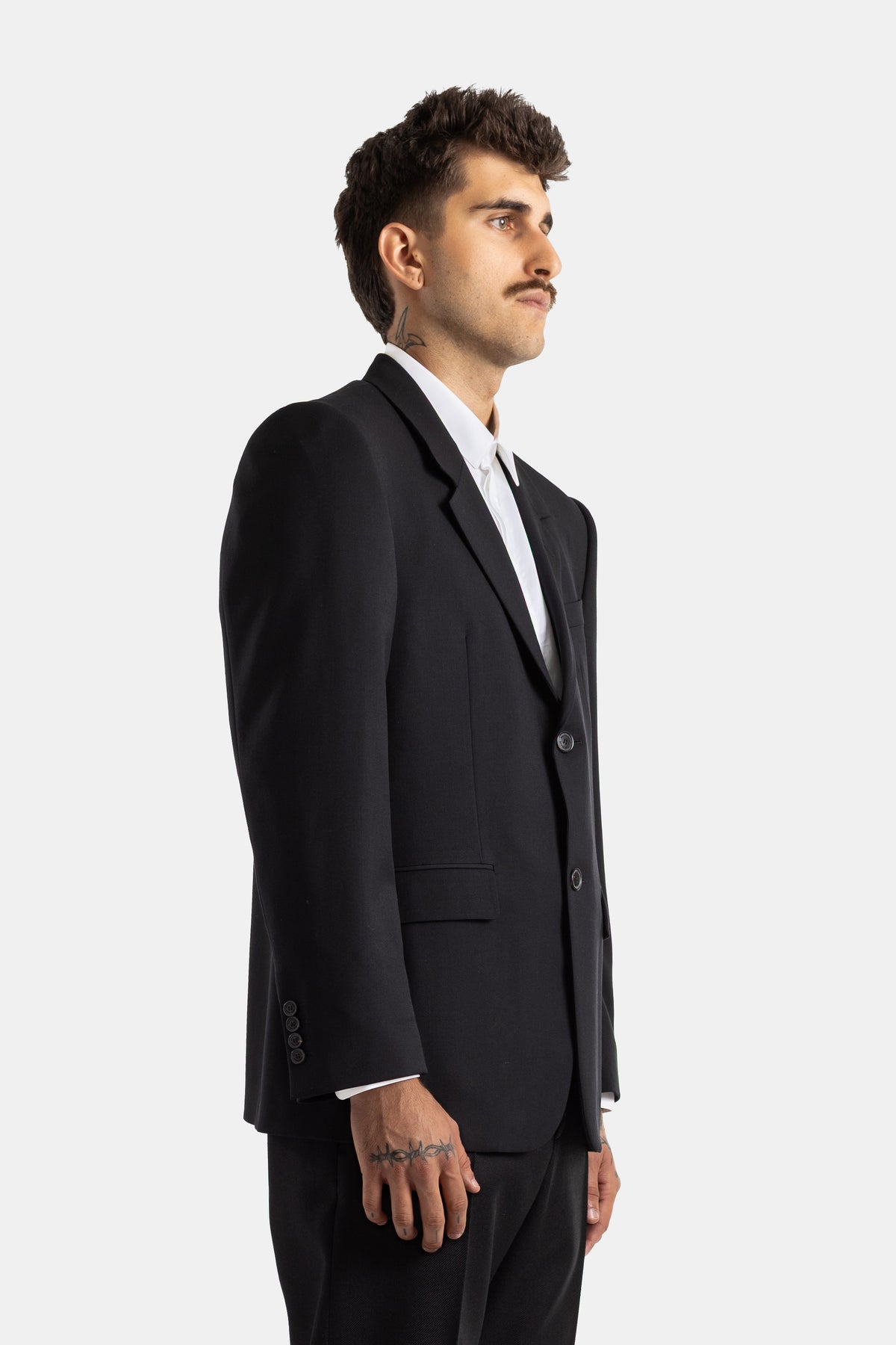 Blazer sartoriale nero Balenciaga visto di profilo con taglio sciancrato e monopetto da uomo con tatuaggi.