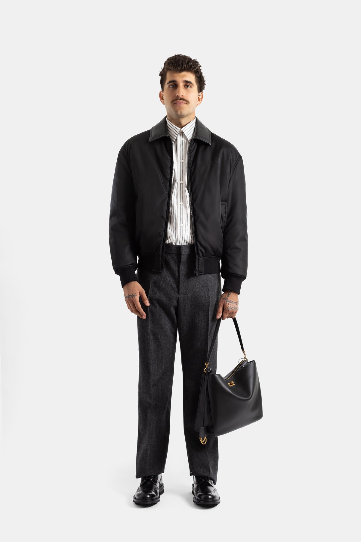 Bomber Balenciaga Cocoon negro con camisa de rayas, bolso de piel negro para un look de hombre elegante.