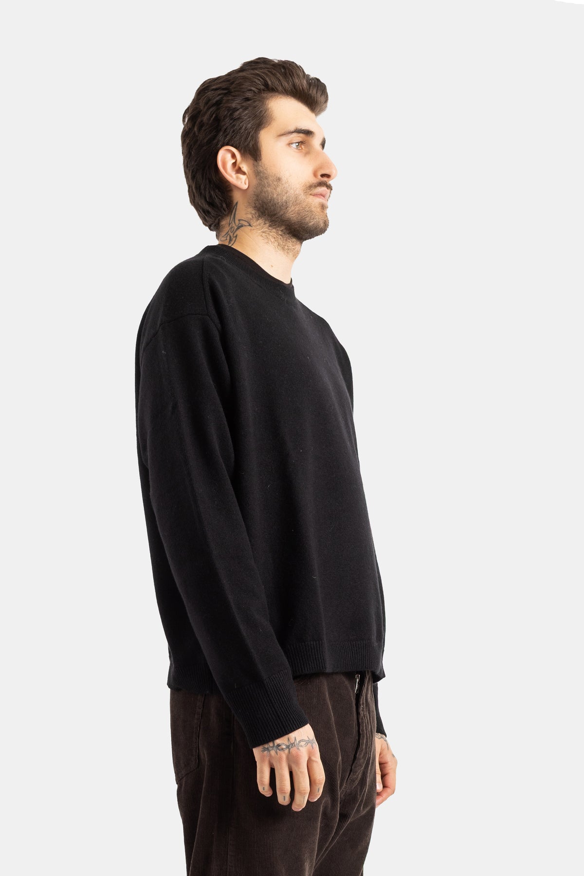 Studio Nicholson Herren-Wollpullover in Schwarz in Seitenansicht mit Rundhals und gerippten Bündchen.