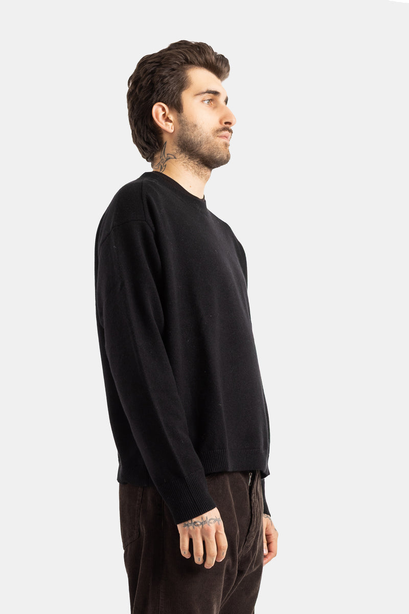 Studio Nicholson Herren-Wollpullover in Schwarz in Seitenansicht mit Rundhals und gerippten Bündchen.