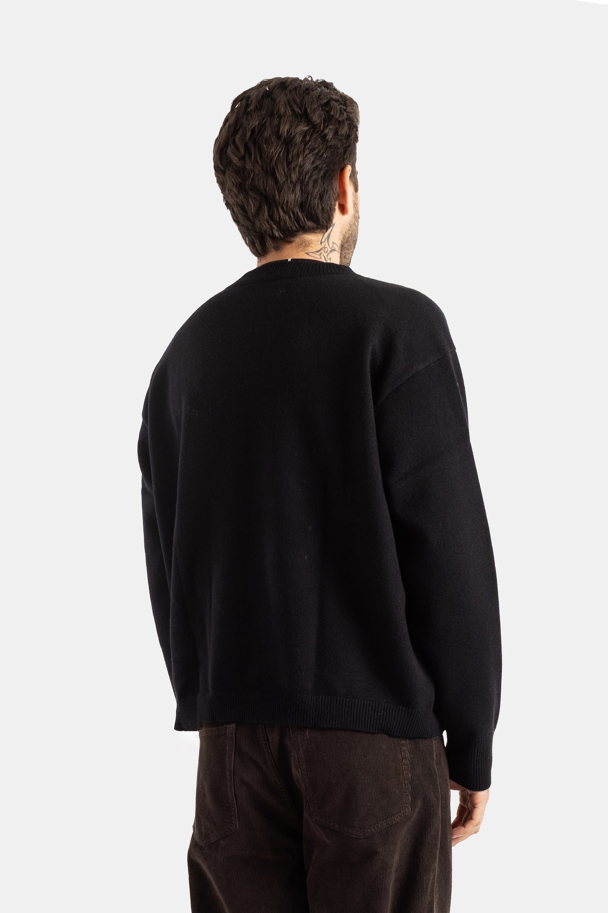 Rückansicht des Studio Nicholson Herren-Wollpullovers in Schwarz mit weiter Passform und Nackentätowierung.