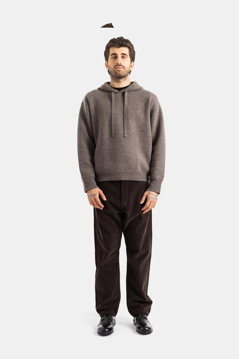 Studio Nicholson Kaschmir-Hoodie in Taupe, kombiniert mit schokoladenbrauner Cordhose und schwarzen Derbies.