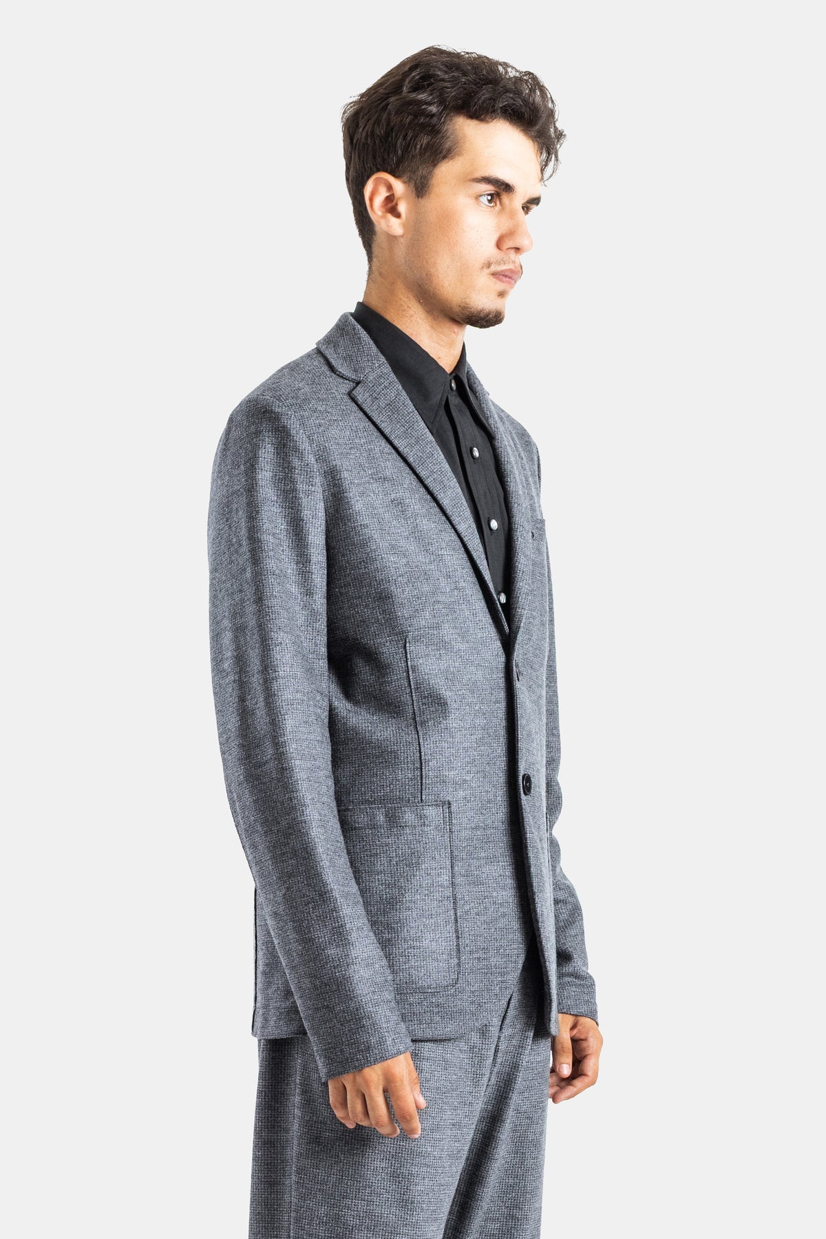 Harris Wharf Herren-Blazer aus grauer Hahnentritt-Wolle in Profilansicht mit aufgesetzten Taschen und schwarzem Hemd.