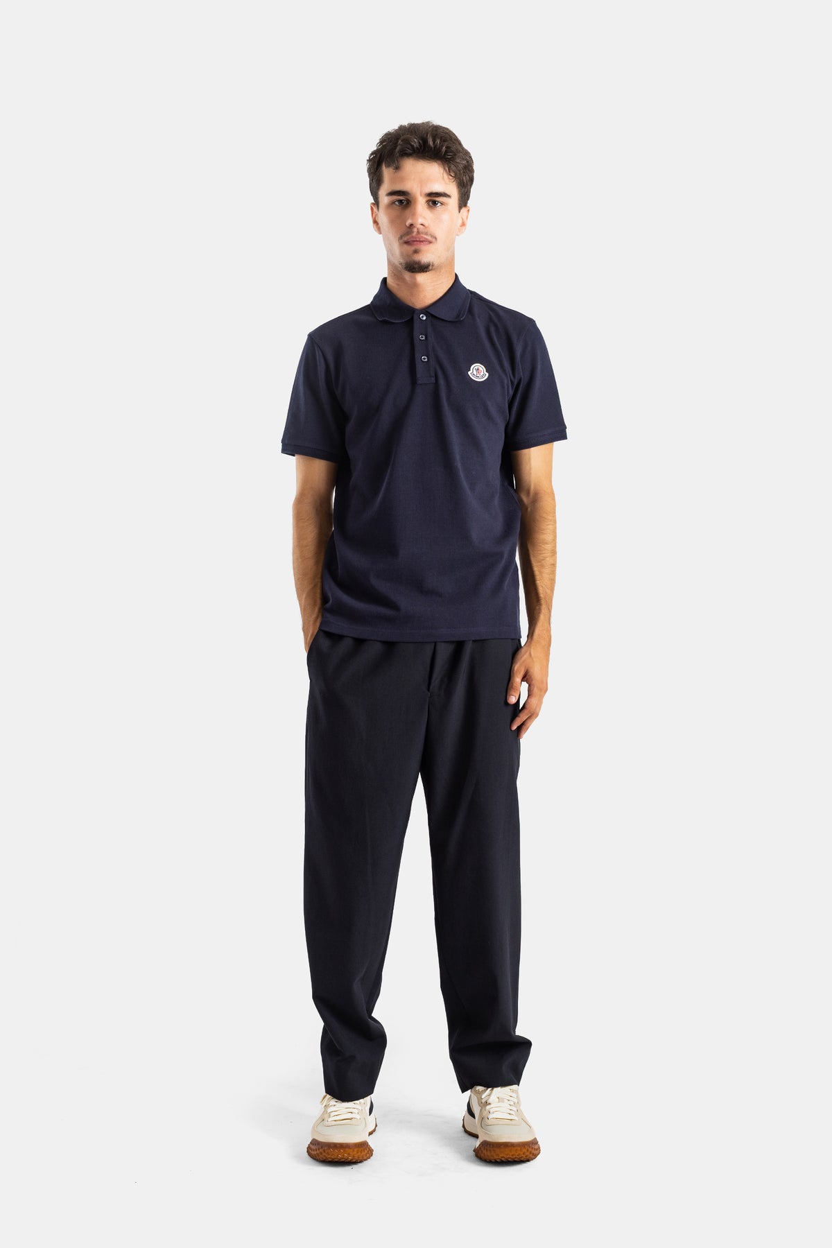 Full look with Moncler navy polo shirt, fluid trousers, white sneakers and iconic chest logo patch for men.