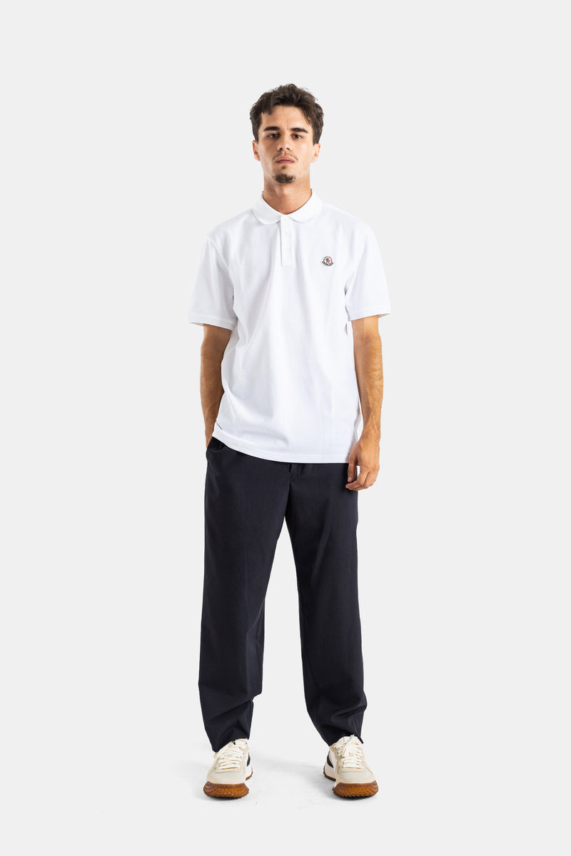 Full front view of a Moncler men's white polo shirt, styled with navy trousers and white designer sneakers.
