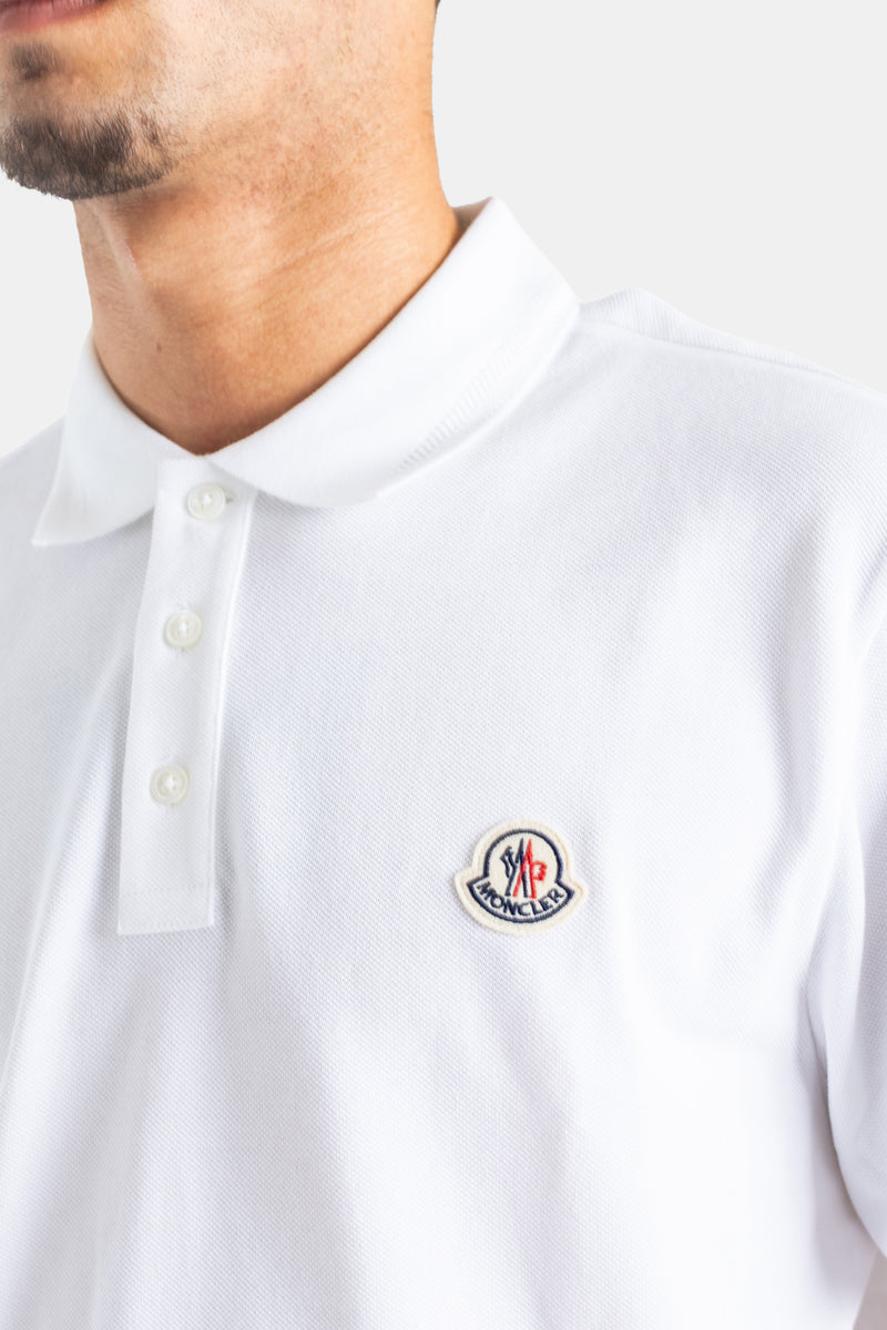 Close-up on Moncler white polo's collar, mother-of-pearl buttons and tricolor embroidered chest logo.