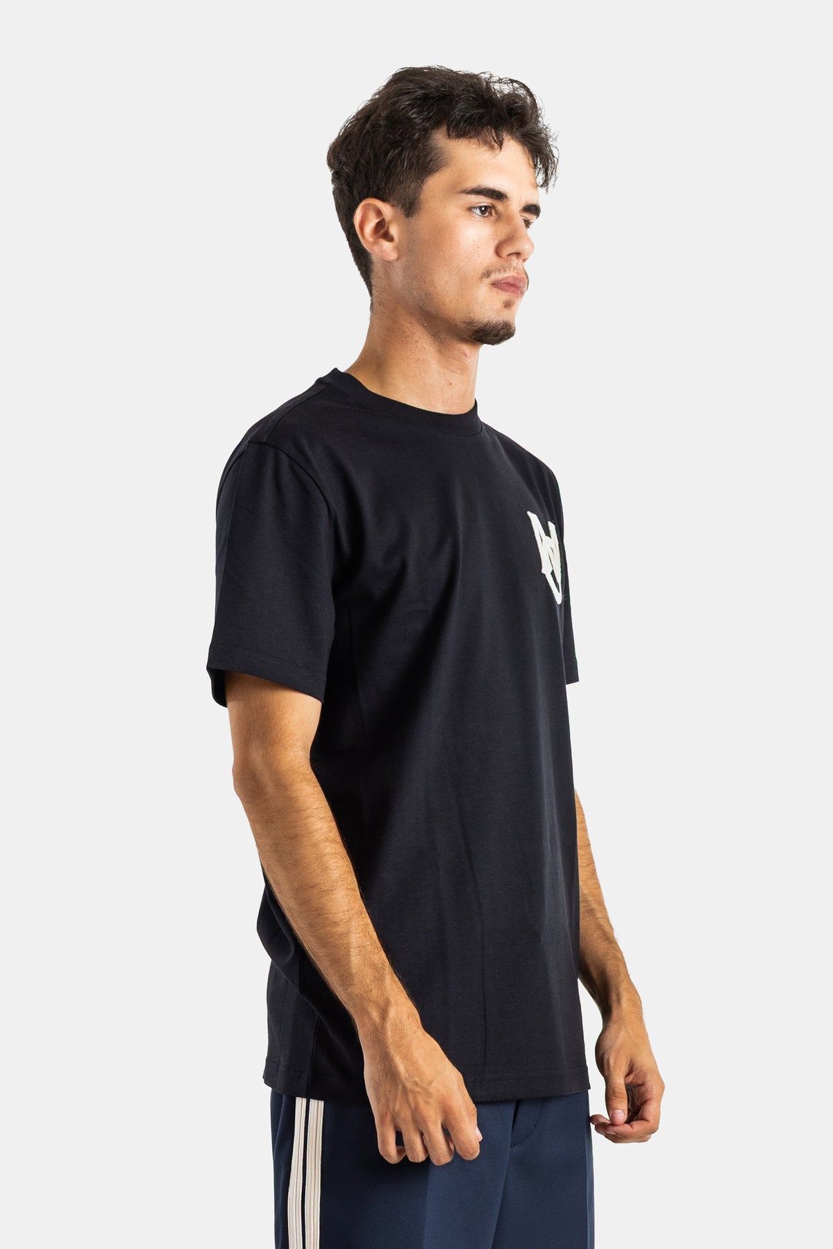 Side profile view of Moncler men's black t-shirt with embroidered chest logo and navy blue sweatpants