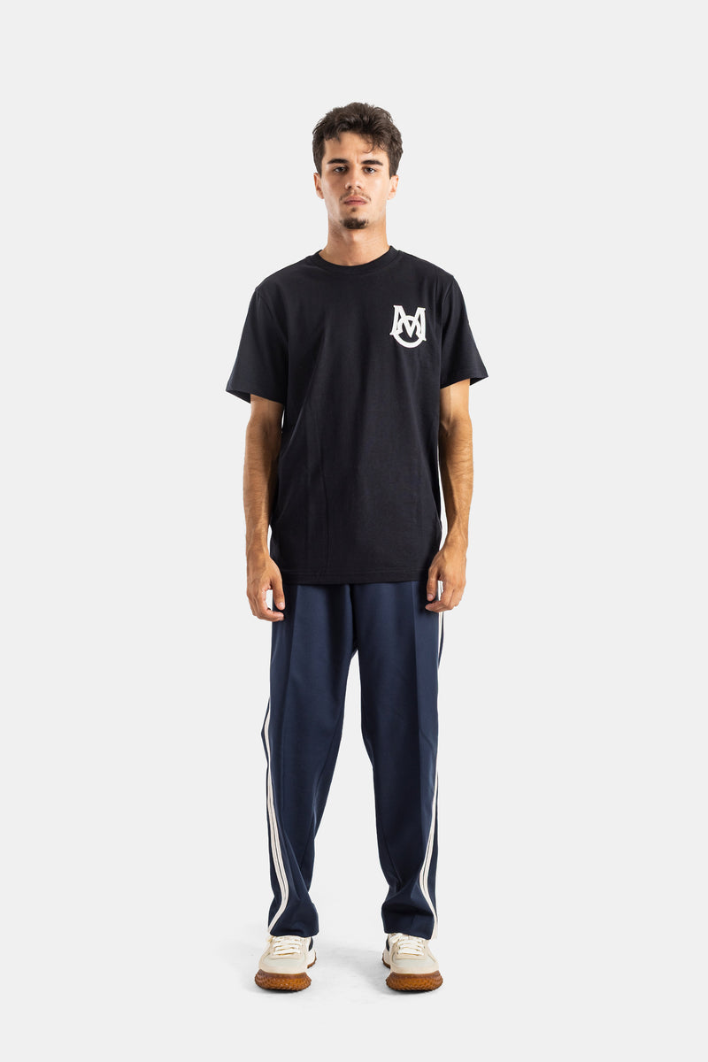 T-shirt preta Moncler com monograma MA no peito e calças de fato de treino azuis com riscas brancas de homem.