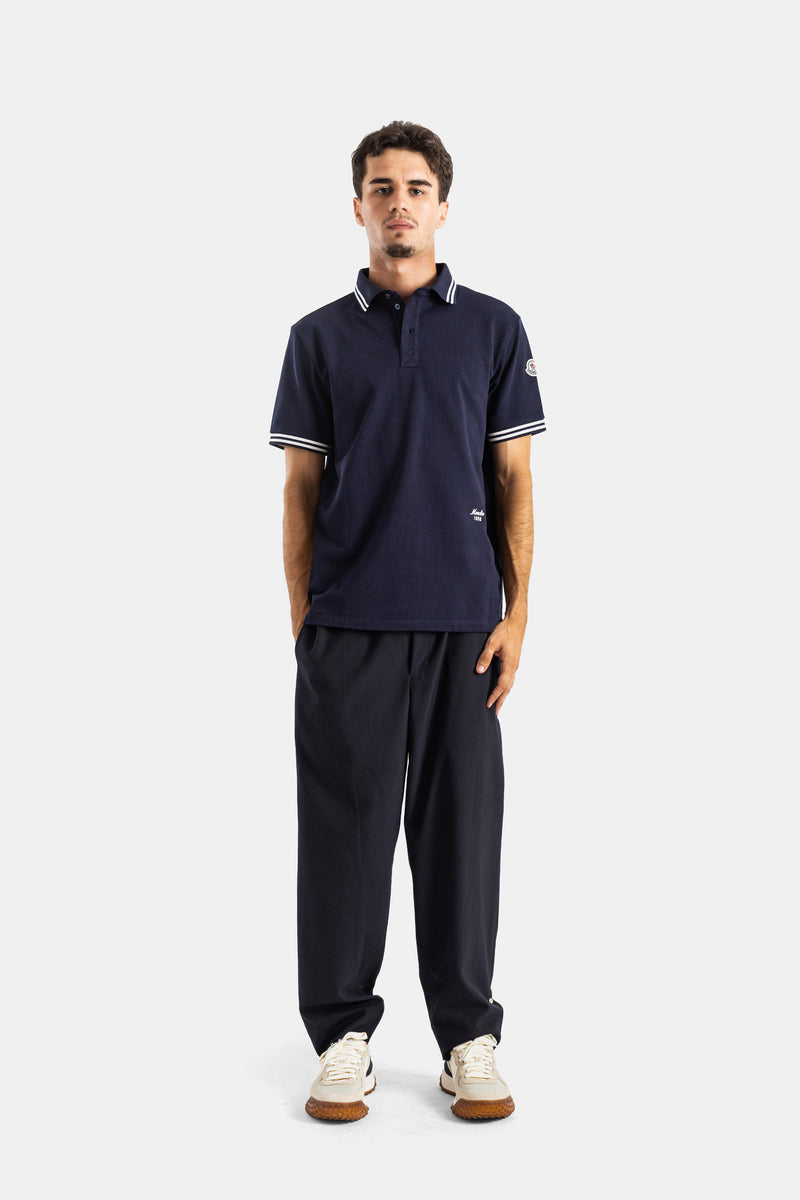 Moncler men's navy blue polo with sleeve logo patch and front script embroidery in a casual chic outfit.