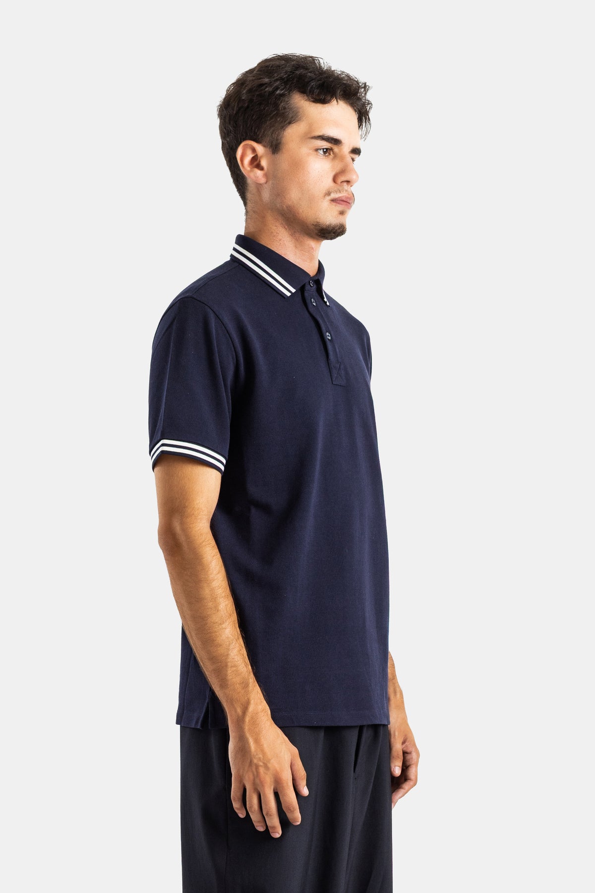 Side profile view of Moncler men's navy blue short-sleeve polo with white stripes on cuffs, relaxed fit.