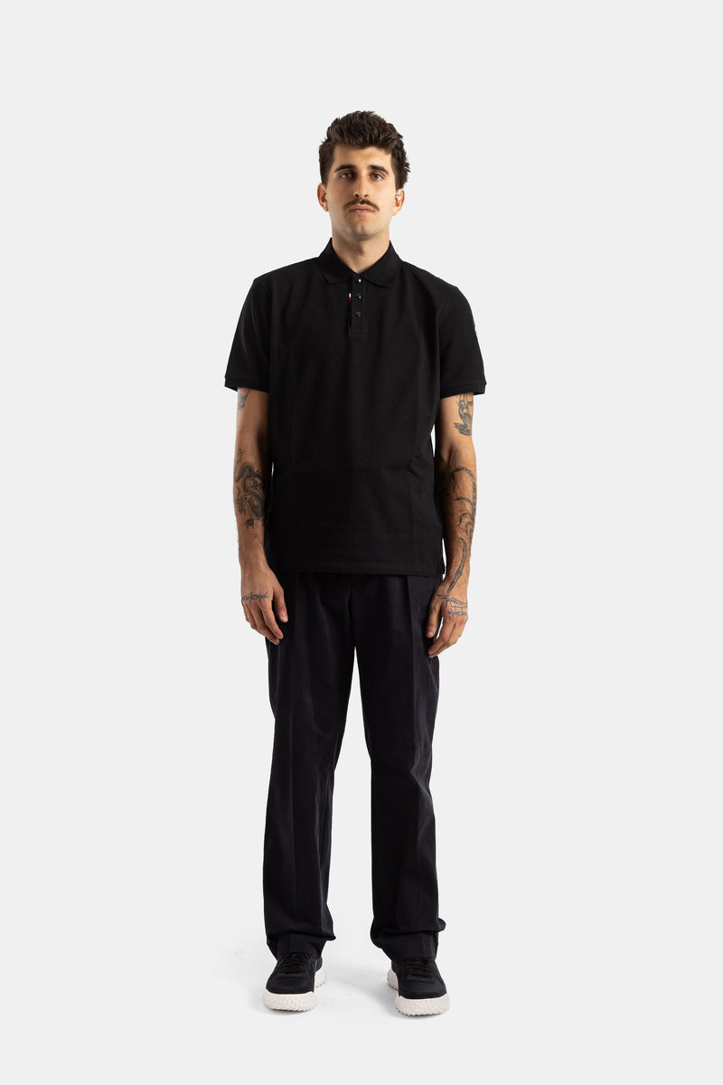 Moncler polo noir manches courtes porté avec pantalon droit coton noir à pinces et sneakers homme