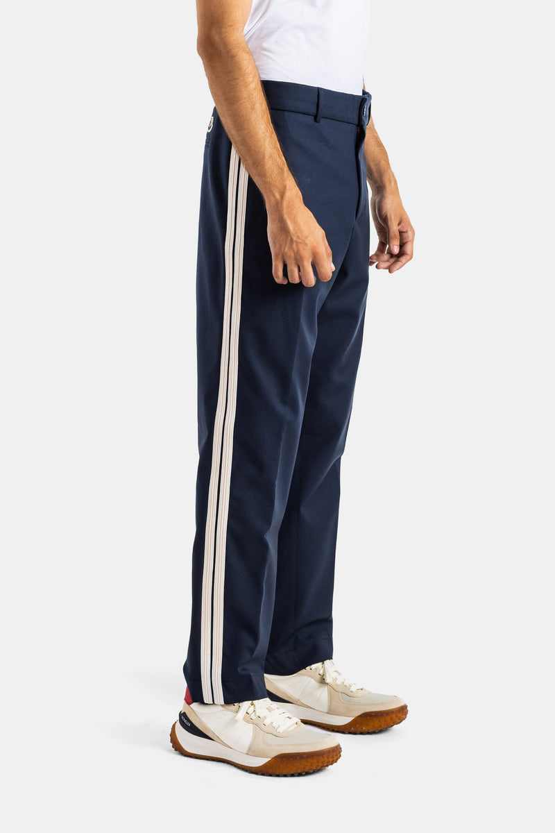 Moncler men's navy blue trousers profile view featuring a double white side stripe and matching sneakers.