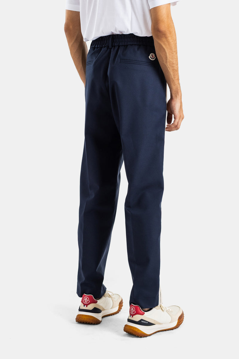 Moncler navy blue trousers with elasticated back waist, logo patch, and white and red running sneakers.