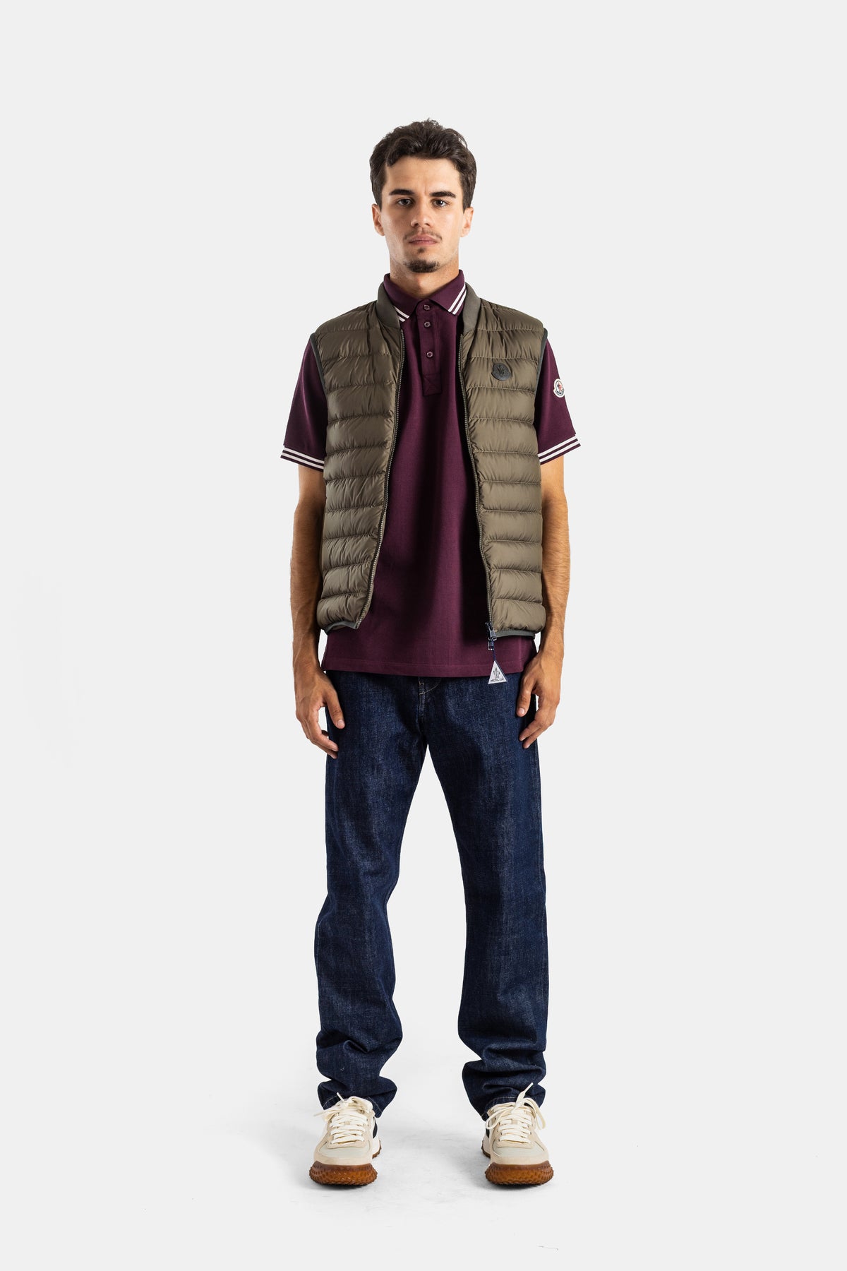 Colete Moncler Froissel sem mangas caqui sobre polo bordeaux e jeans brutos, look casual de luxo masculino.