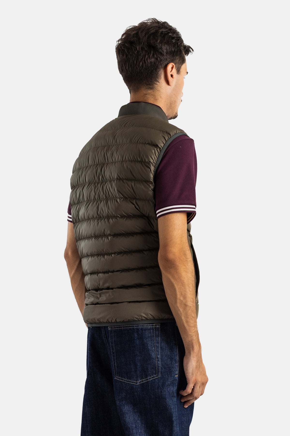 Colete Moncler Froissel sem mangas com costas acolchoadas em caqui-oliva, usado com polo bordeaux às riscas.