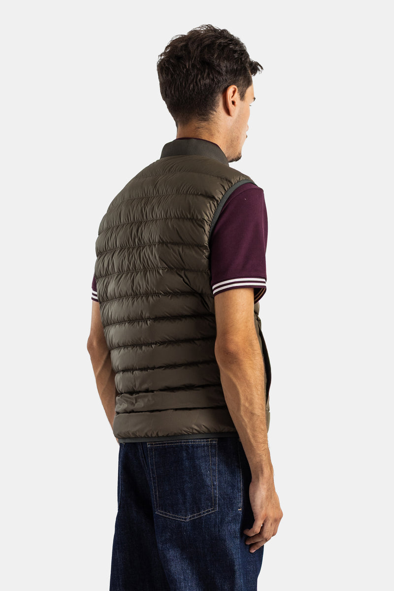 Colete Moncler Froissel sem mangas com costas acolchoadas em caqui-oliva, usado com polo bordeaux às riscas.