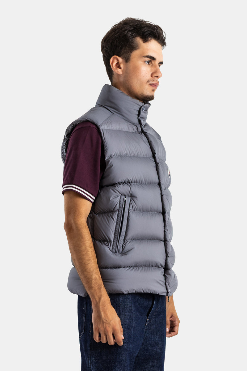 Moncler men's grey sleeveless Tibb down jacket in side profile, featuring horizontal quilting and a zip pocket.