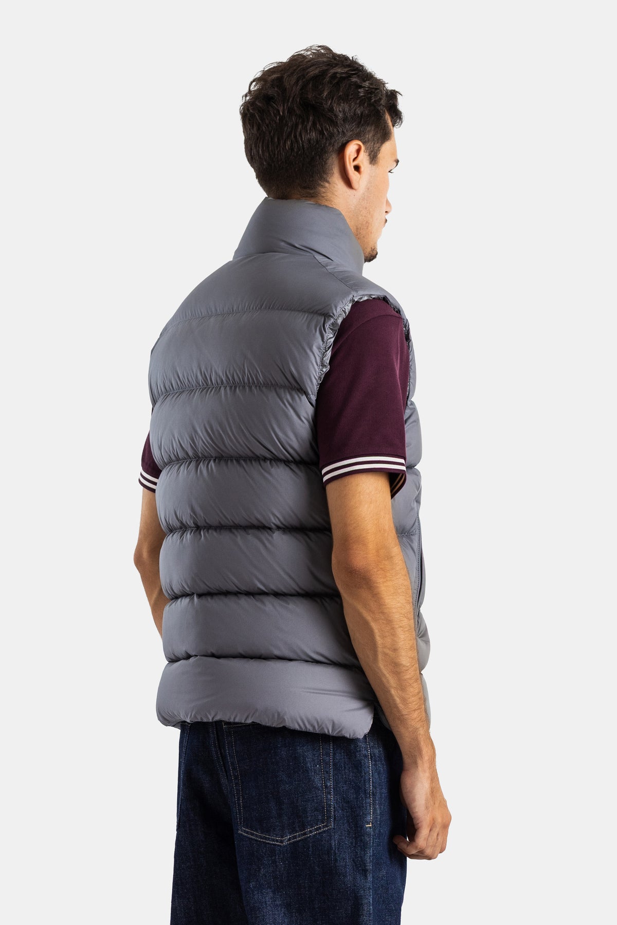 Three-quarter back view of Moncler's grey Tibb down vest for men, showing horizontal quilting and a funnel neck.