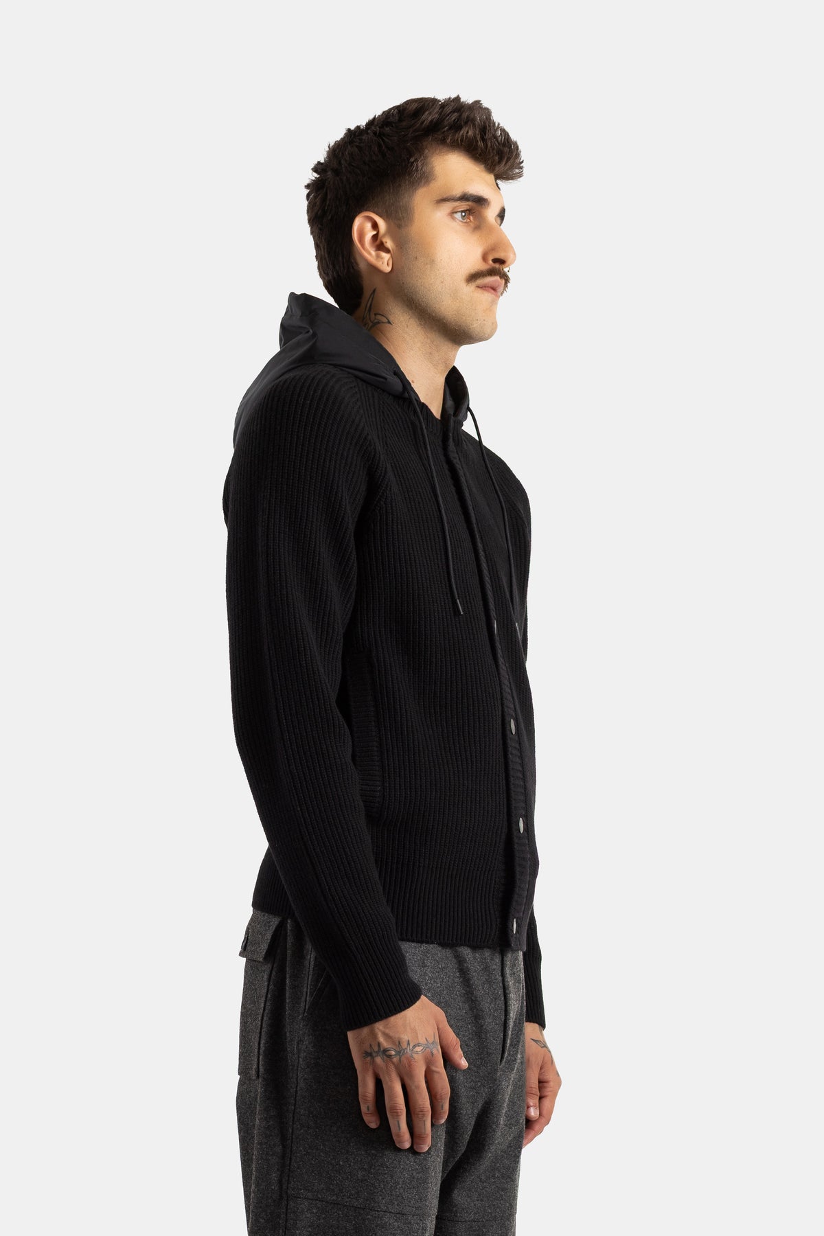 Profile view of Moncler men's black cardigan, nylon hood with drawstrings, paired with grey cargo pants.
