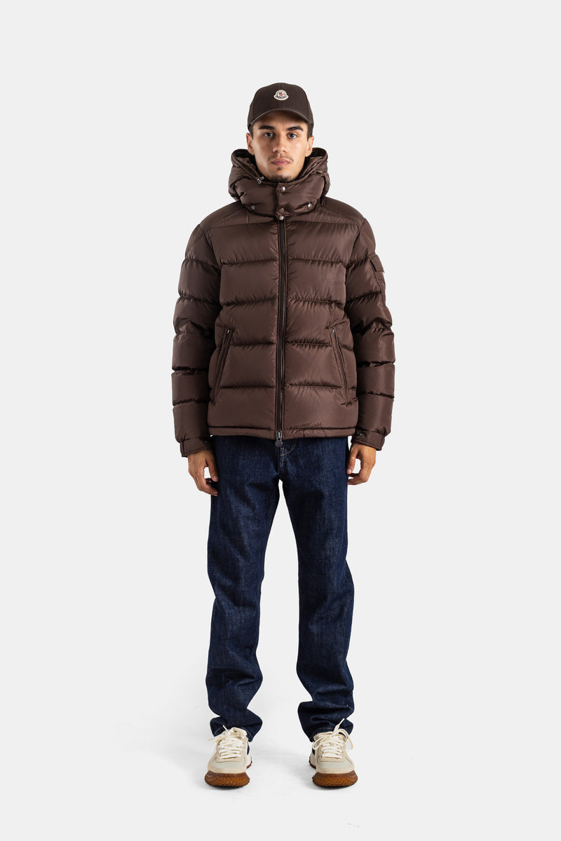 Look casual Moncler Maya homem silhueta completa com jeans brutos sapatilhas brancas e casaco mate castanho