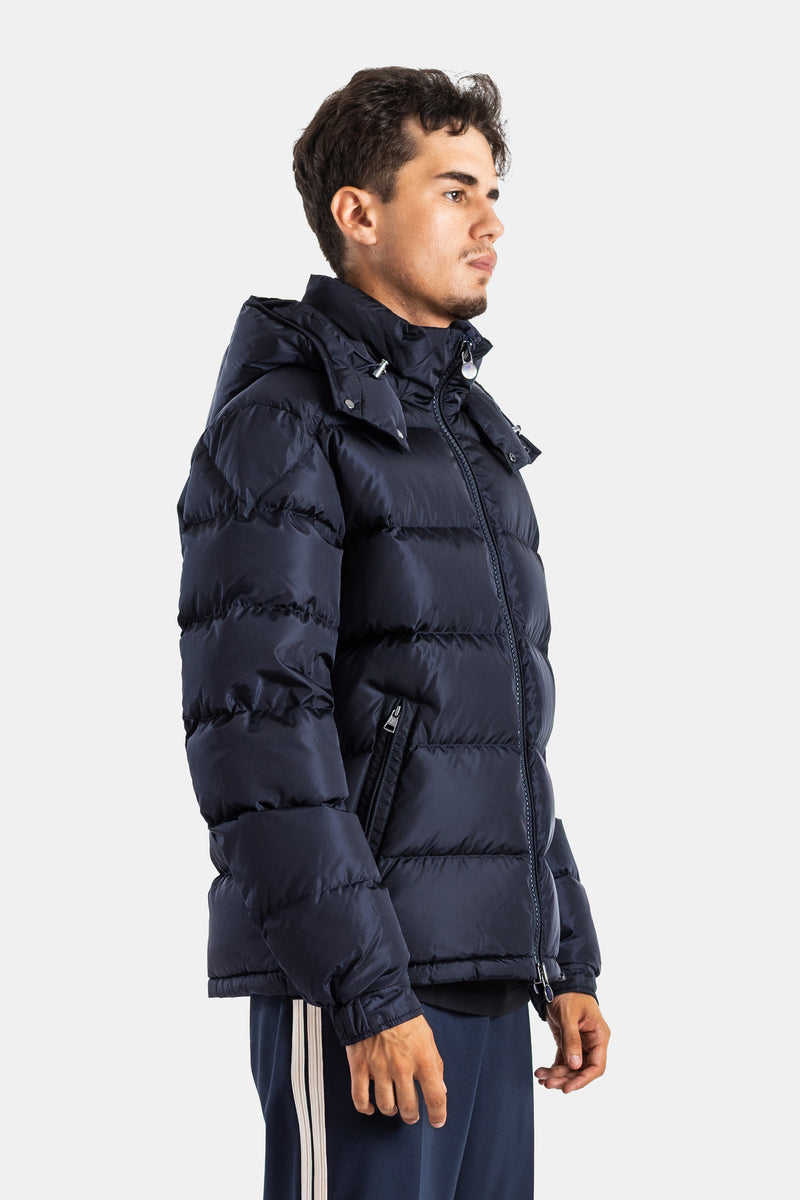 Side profile of Moncler Maya men's quilted down jacket in matte navy blue with a zipped pocket and large hood.