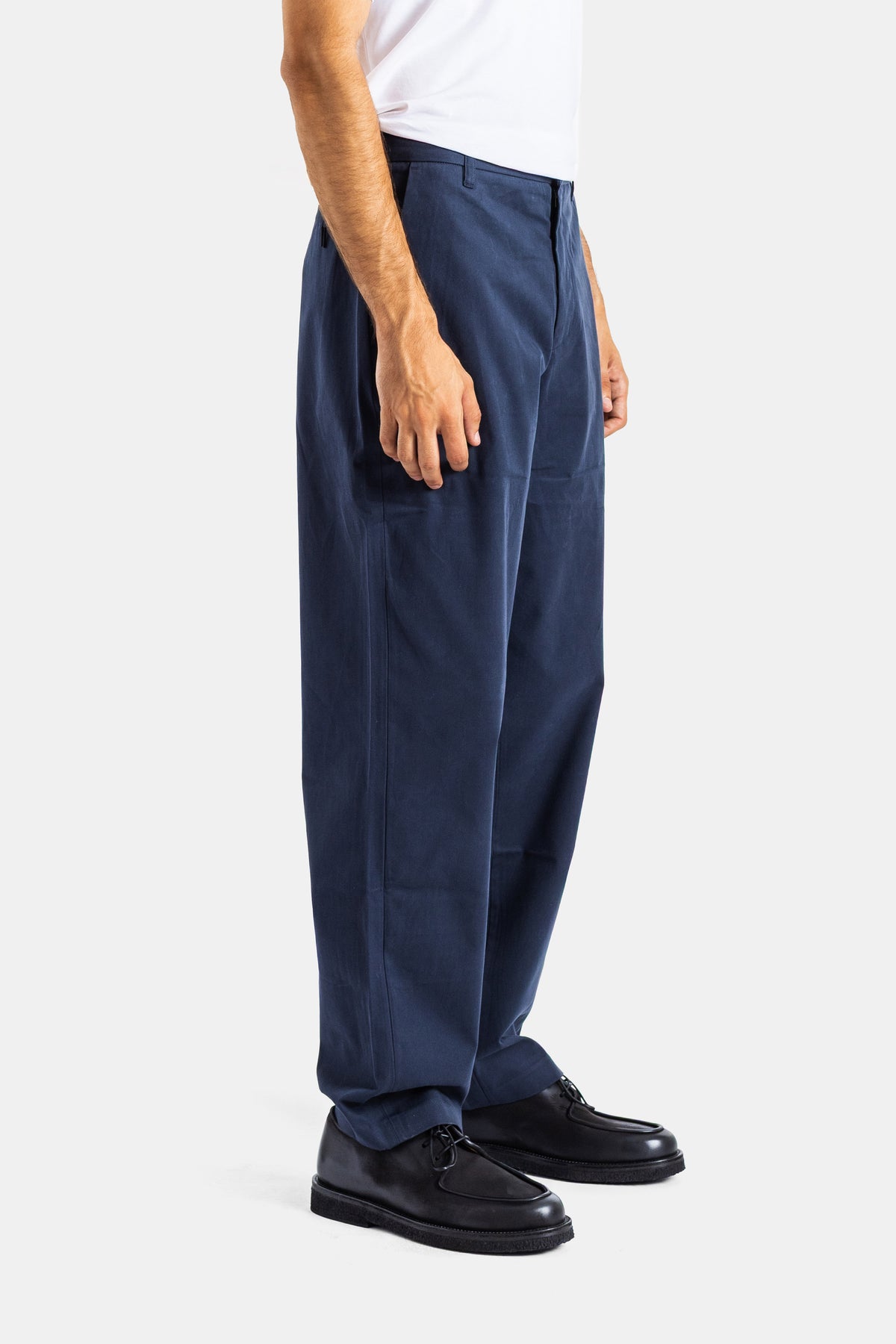 Side view of Sease men's navy blue chino pants with pleats, styled with black leather derby shoes.