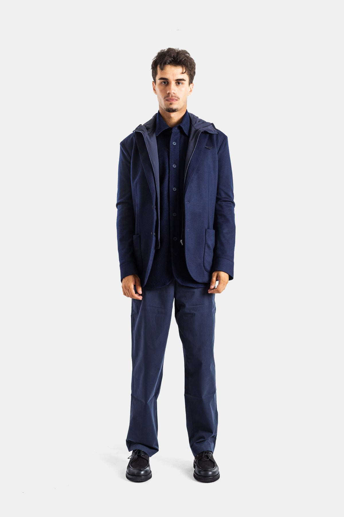Sease navy hybrid blazer in a total navy look, layered with a hooded gilet, straight pants and black derbies.