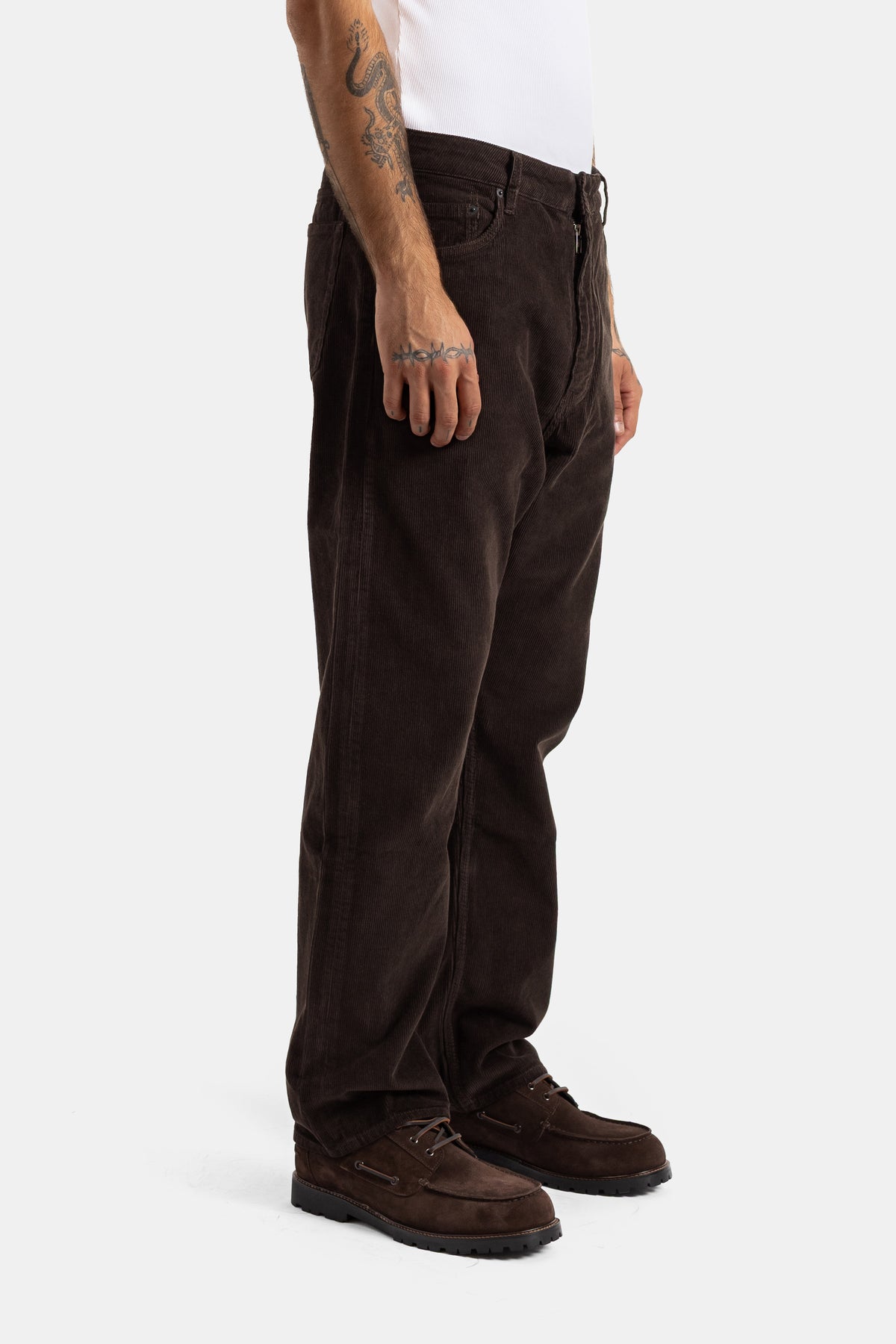 Side view of Studio Nicholson brown corduroy trousers with high waist and straight cut, worn with suede loafers.