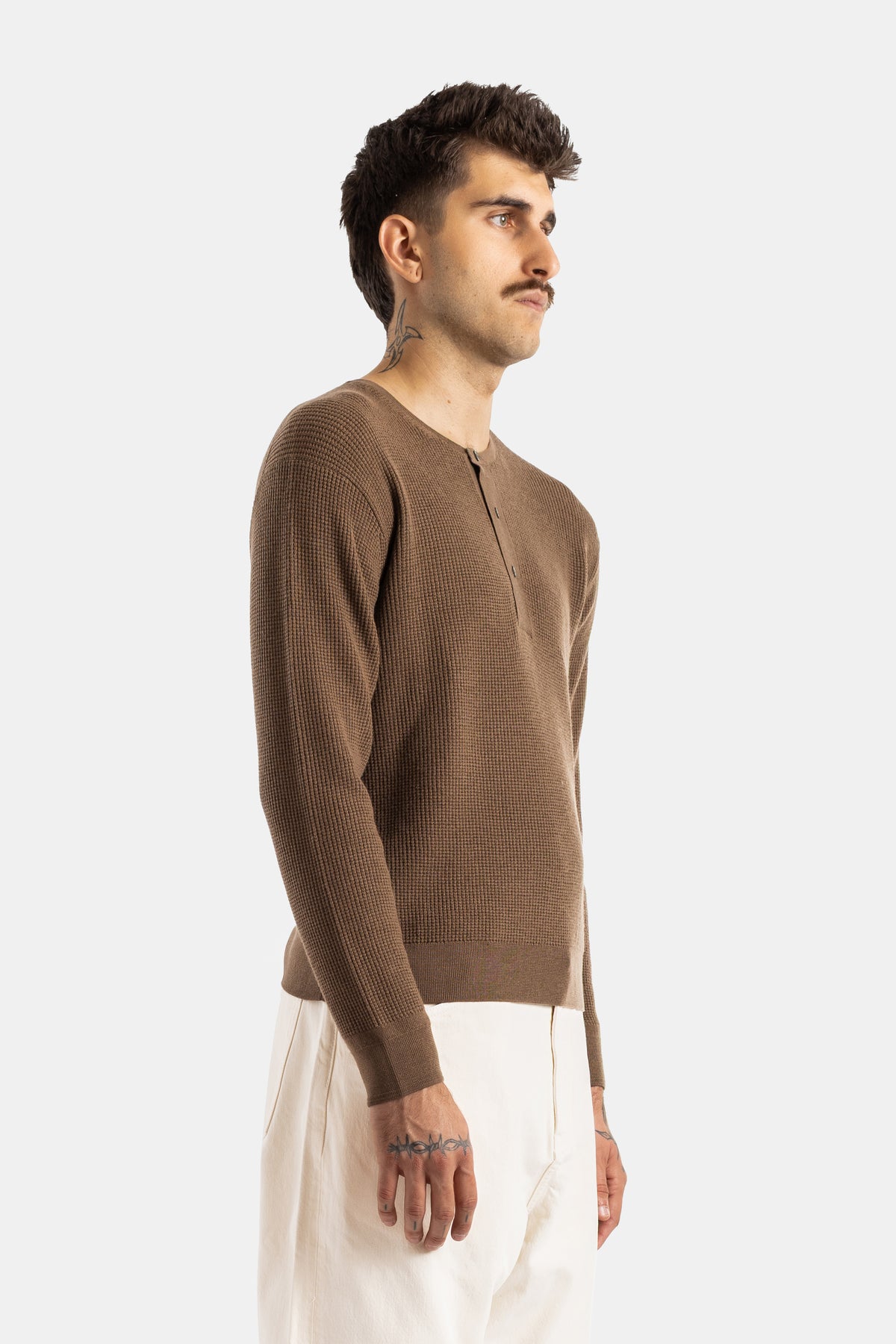 Side view of Studio Nicholson men's waffle-knit henley in camel brown worn with cream-white trousers.