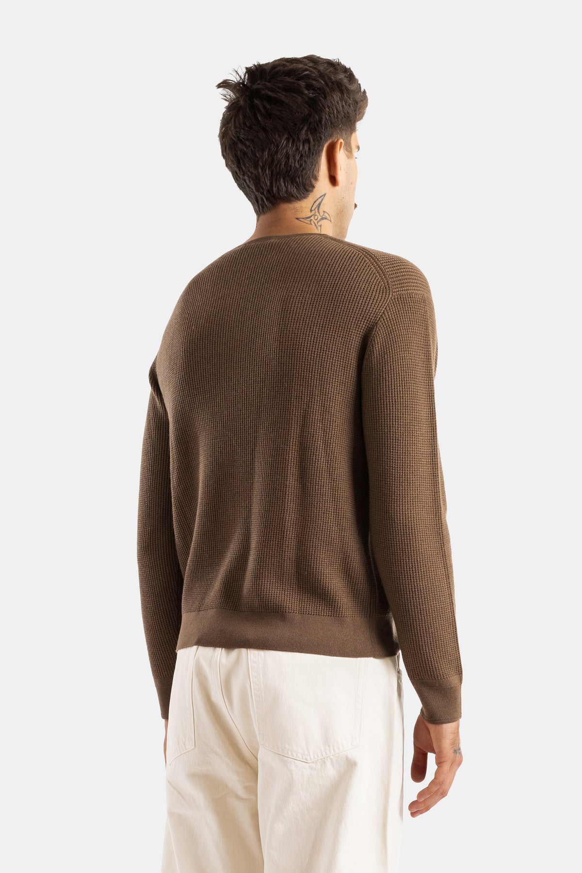Back view of Studio Nicholson brown waffle-knit henley sweater showing the crew neck and ecru trousers.