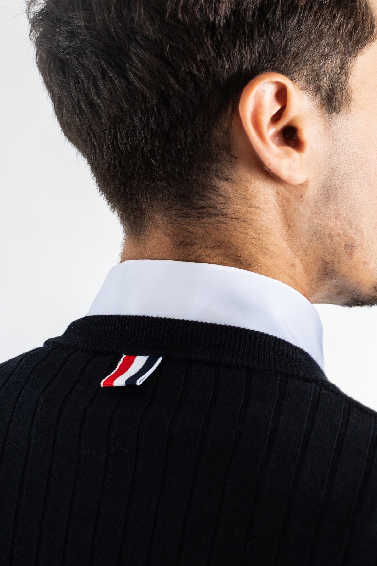 Thom Browne Merinowollpullover in Schwarz mit gestreifter RWB-Lasche am Kragen über einem weißen Hemd.